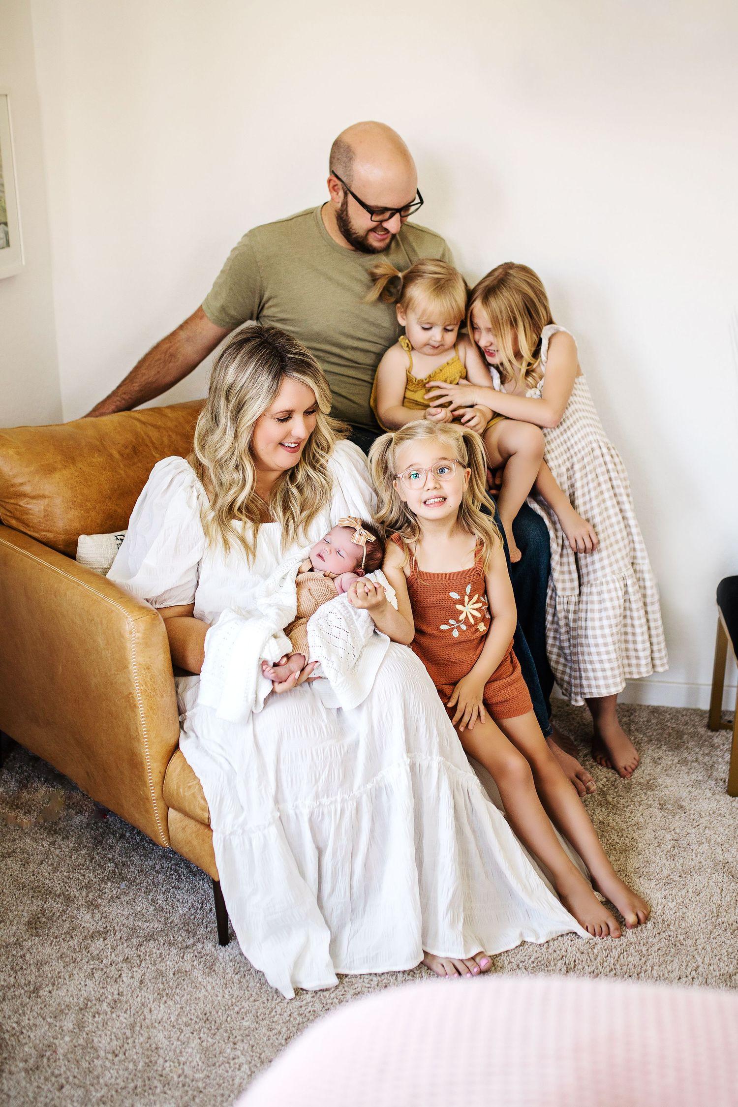 Happy family of six sitting together on a leather couch with a newborn baby.