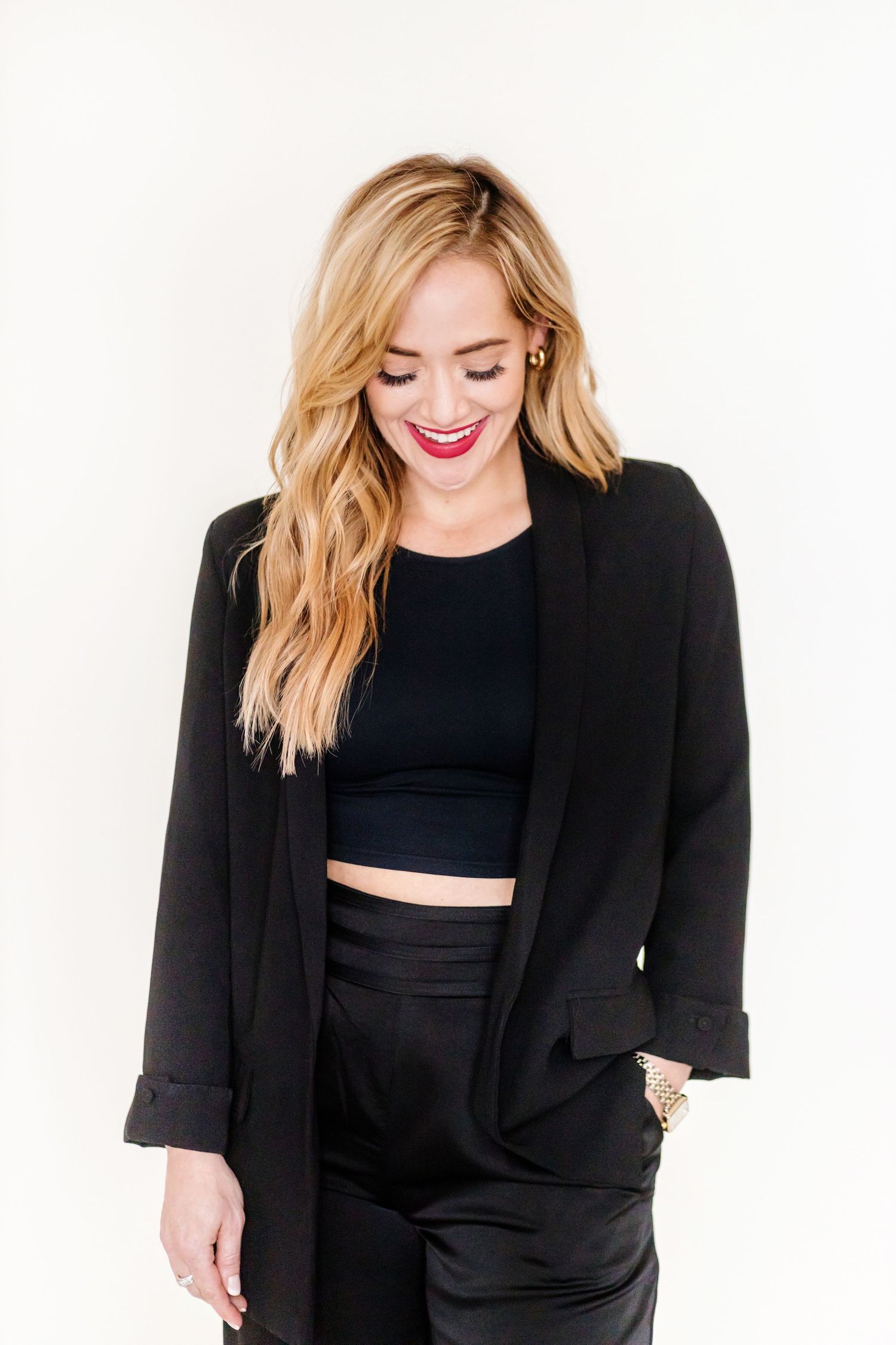 Stylish woman in all black outfit with crop top and blazer smiling.