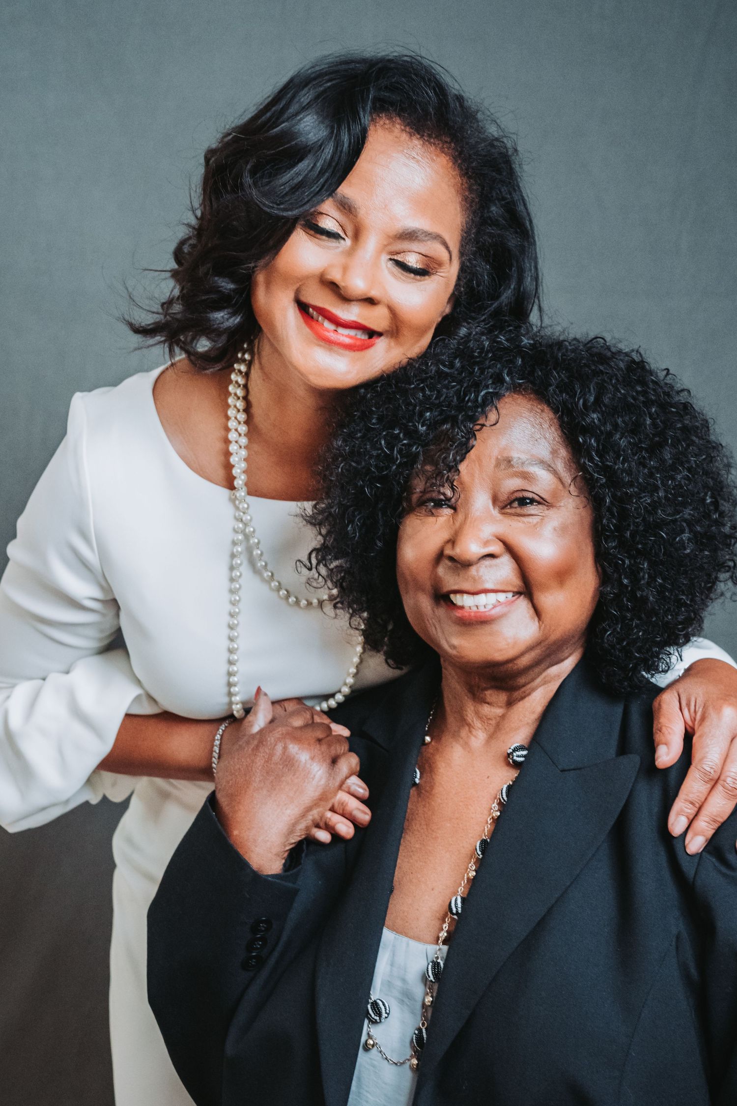 Two smiling Black women posing together in elegant attire for professional portrait photo.