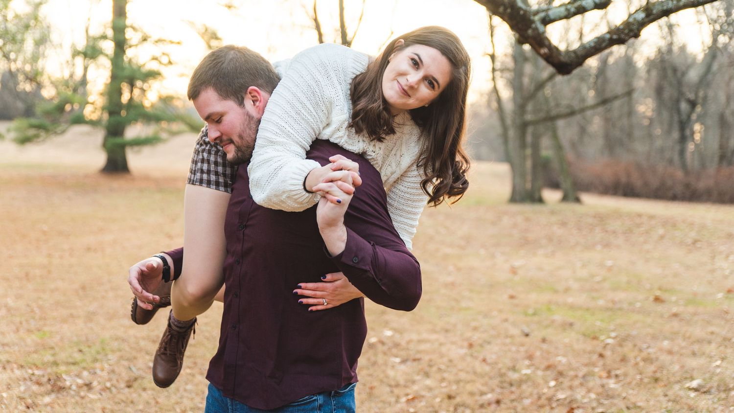 A newly engaged couple, she is on his back and displaying her engagement ring.
