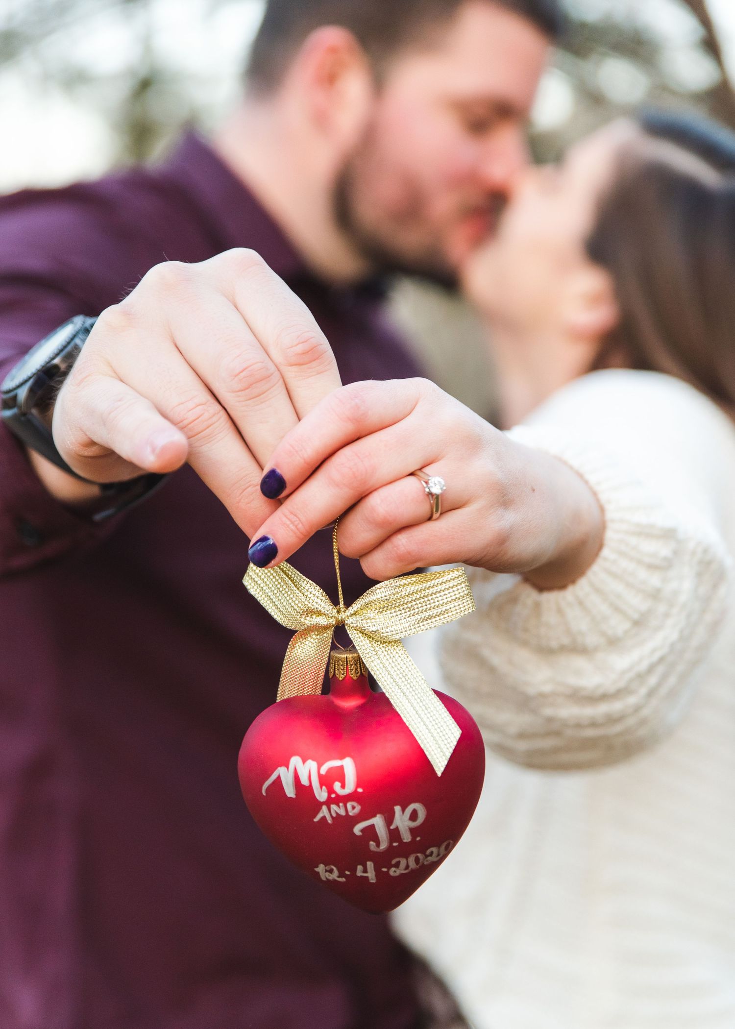 A newly engaged couple kissing holding a Christmas ornament with their wedding date.