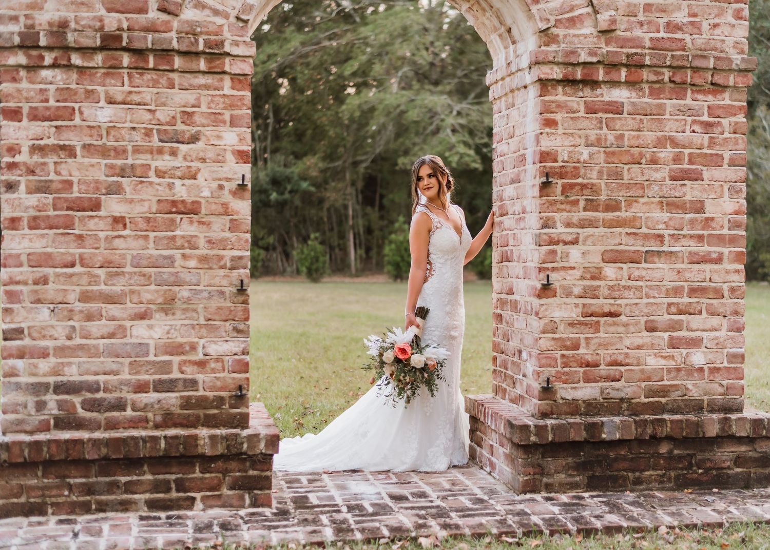 Panoramic view of bride in white dress standing by vintage brick architecture.