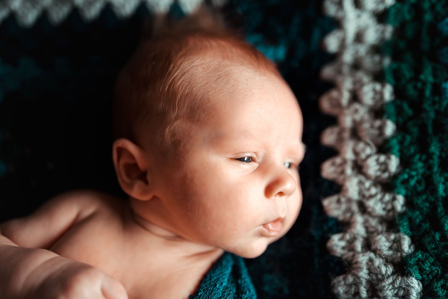 Close-up artistic newborn photography with teal bokeh lighting effects in the background.