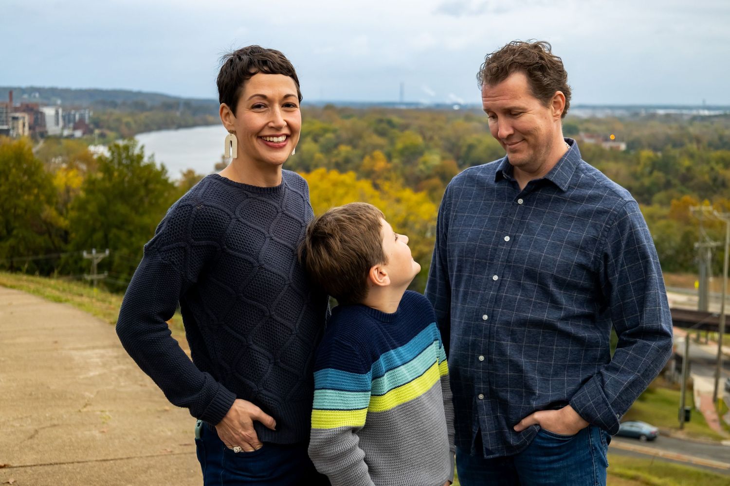 Three people share a candid moment together on a hilltop overlooking a fall landscape.