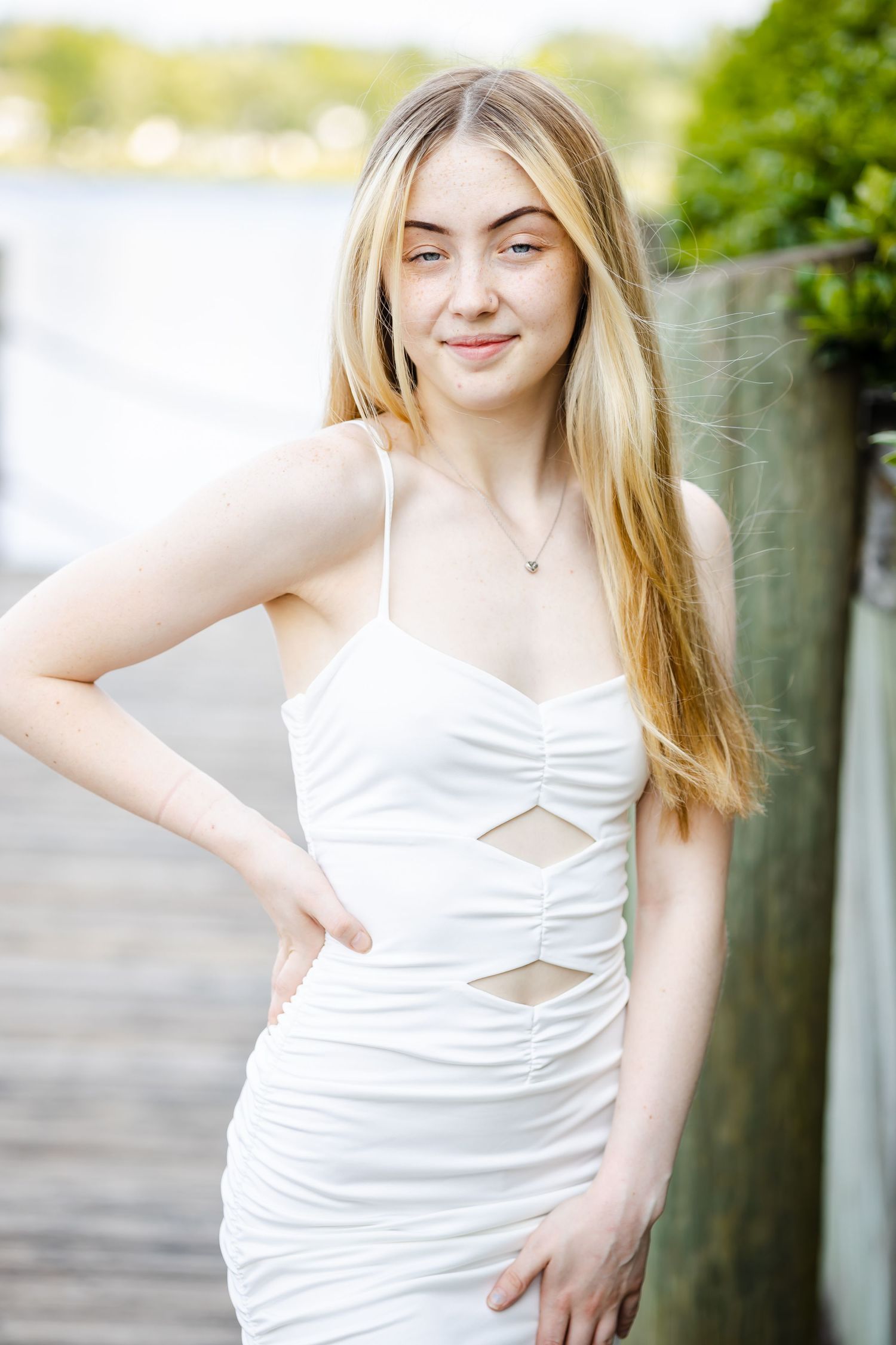 Graduate in white dress poses casually on boardwalk during summer photo session.