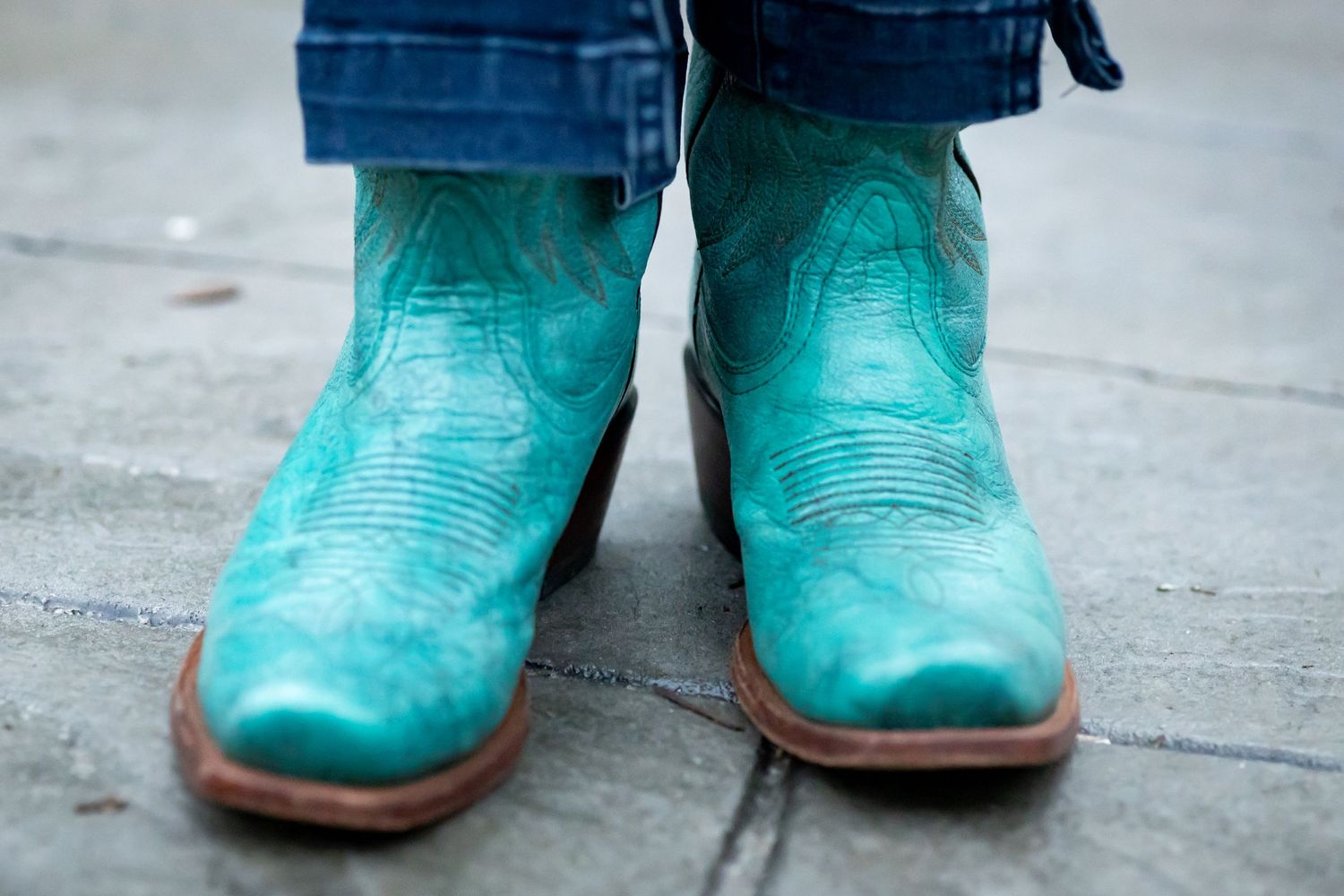 Close-up of turquoise leather cowboy boots with detailed stitching on concrete.