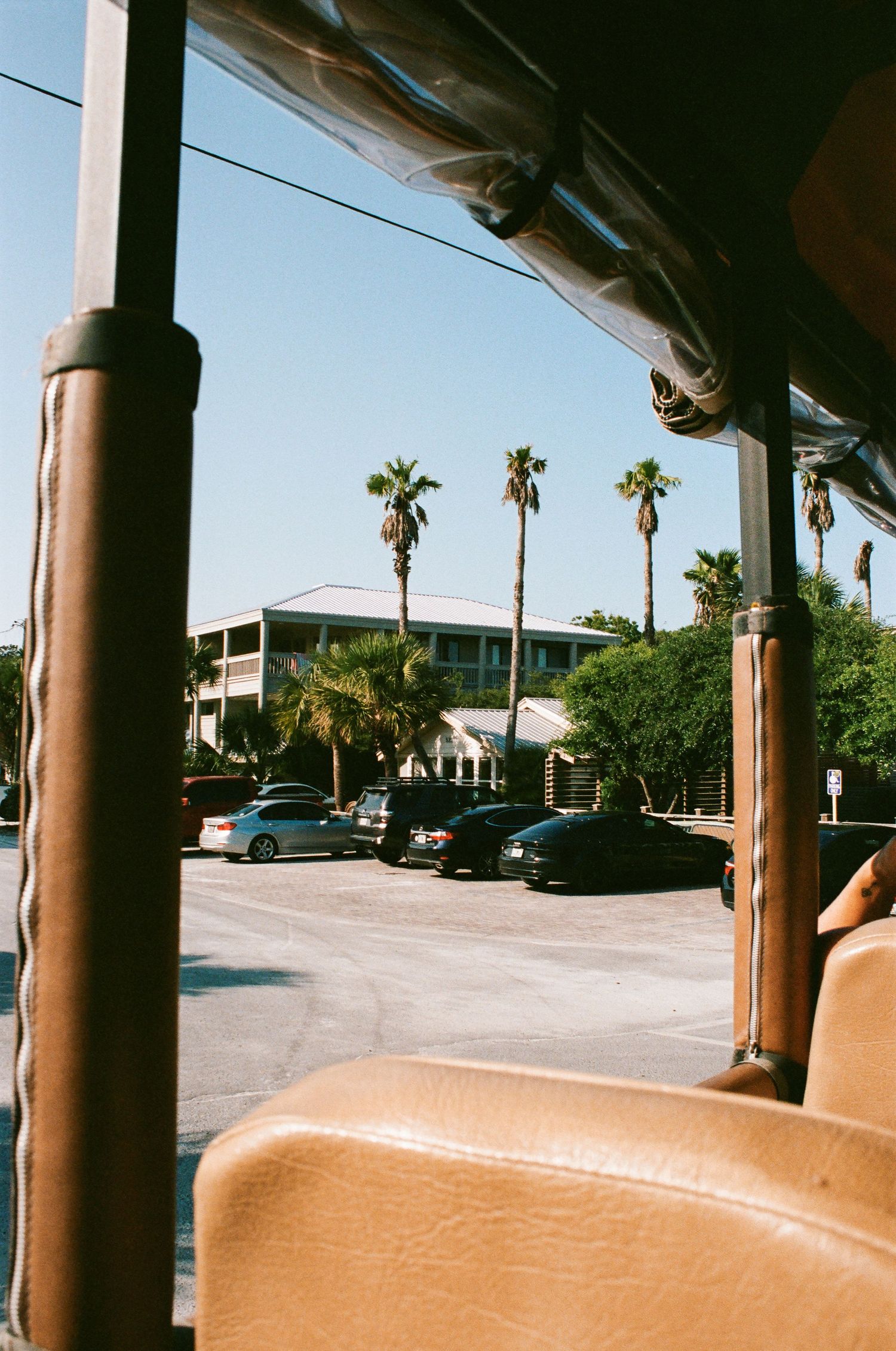 Interior view of a beach vehicle with tan seats and palm trees visible through windshield.