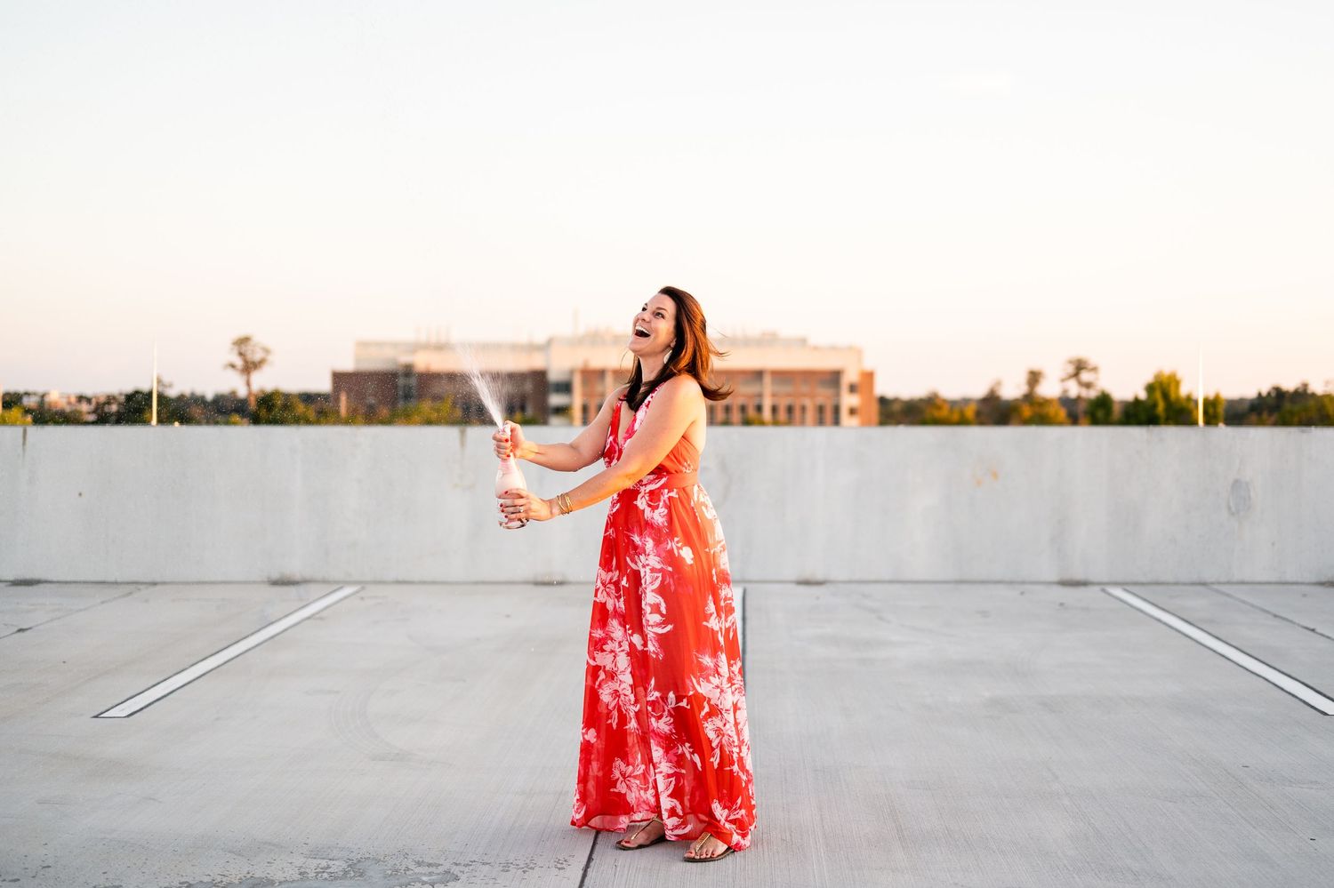 Woman wearing a red floral maxi dress celebrates with champagne on a rooftop.