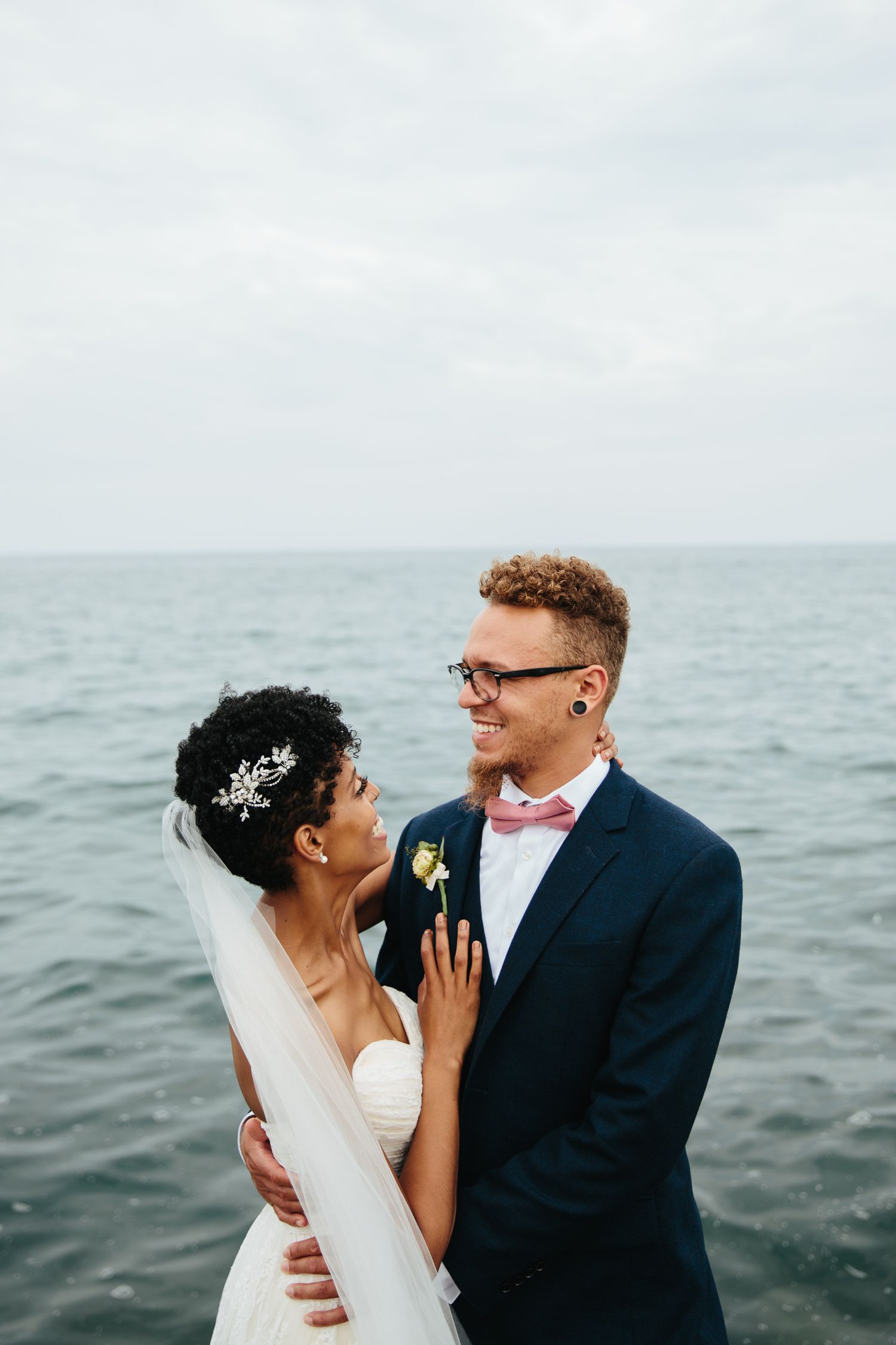 black couple in wedding attire laugh in front of lake michigan