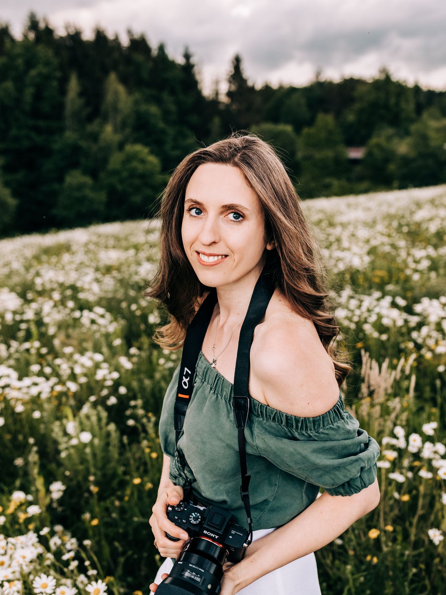 Photographer with camera in green top poses in blooming wildflower field.