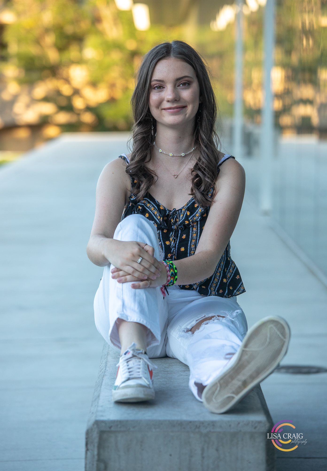 A casual portrait of someone sitting on concrete wearing distressed white jeans and a patterned top.