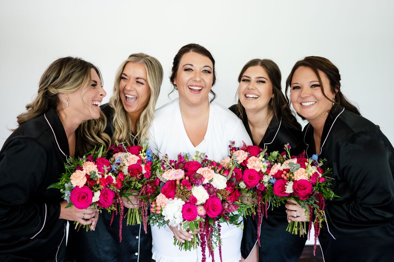 Bridal party holding vibrant pink and white floral bouquets against white background.