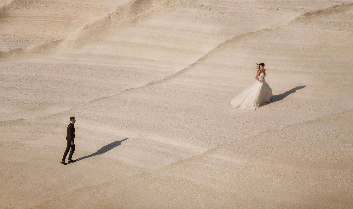 Minimalist desert landscape with long shadows cast on smooth sand dunes.