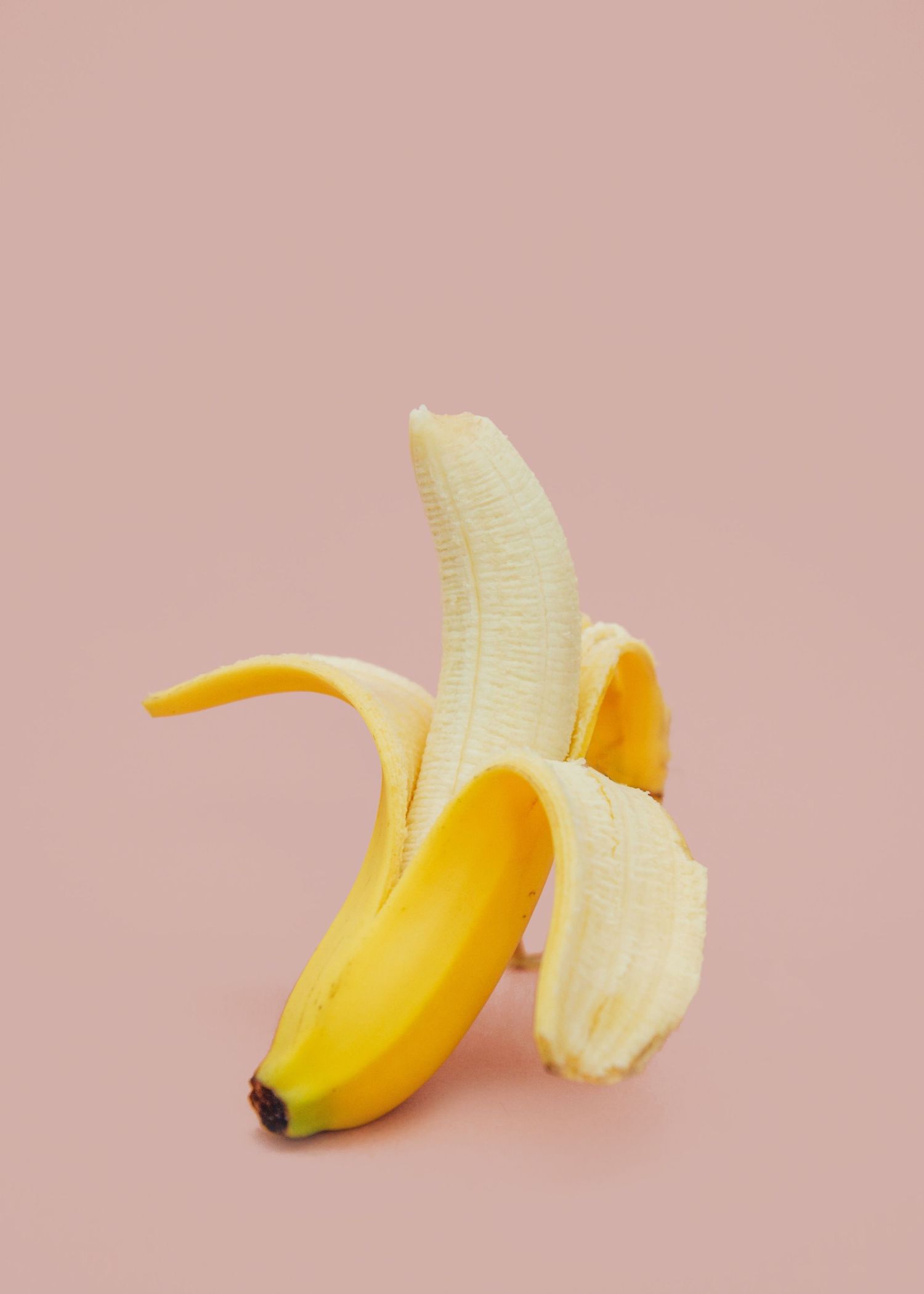A partially peeled ripe banana against a soft pink background in minimalist style.