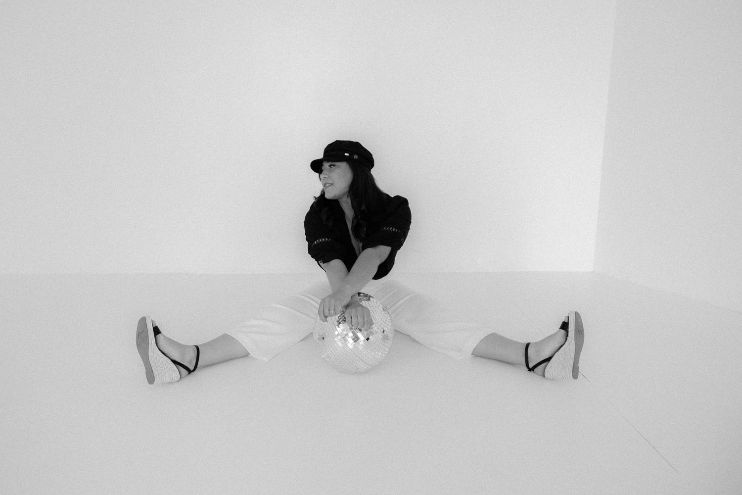 Black and white photo of woman in cap sitting on floor with disco ball.