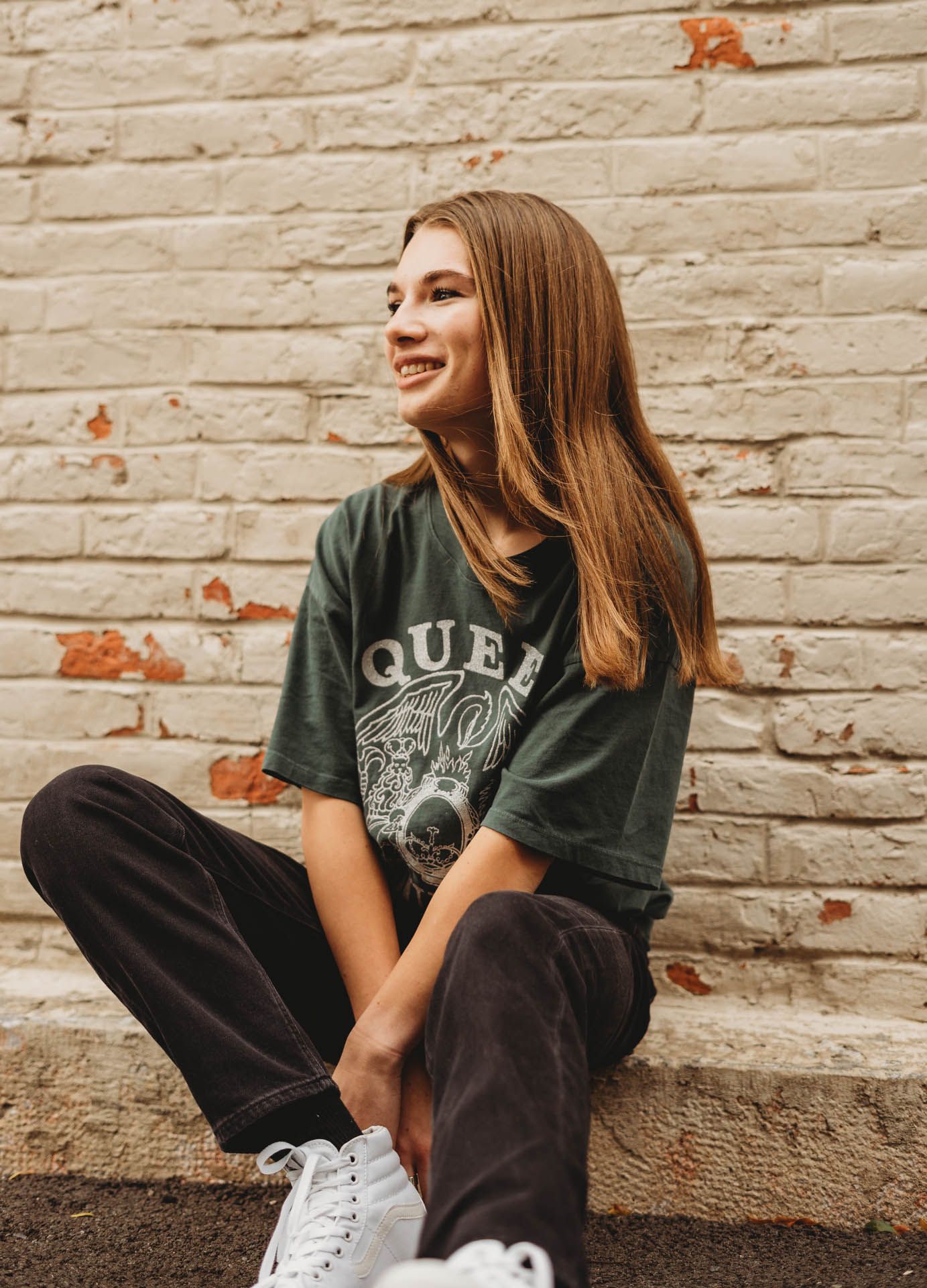 Someone wearing a vintage Queen band t-shirt sits casually against a brick wall.