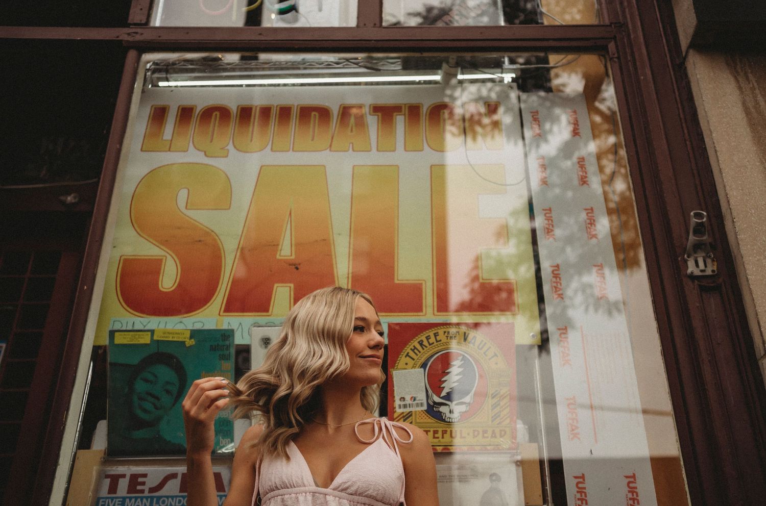 A pink outfit against a storefront window displaying a bright liquidation sale sign.