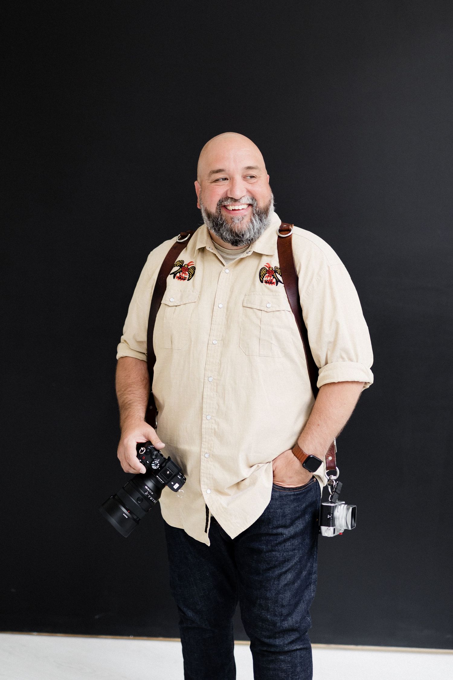 Professional photographer with cameras wearing light shirt against dark background.