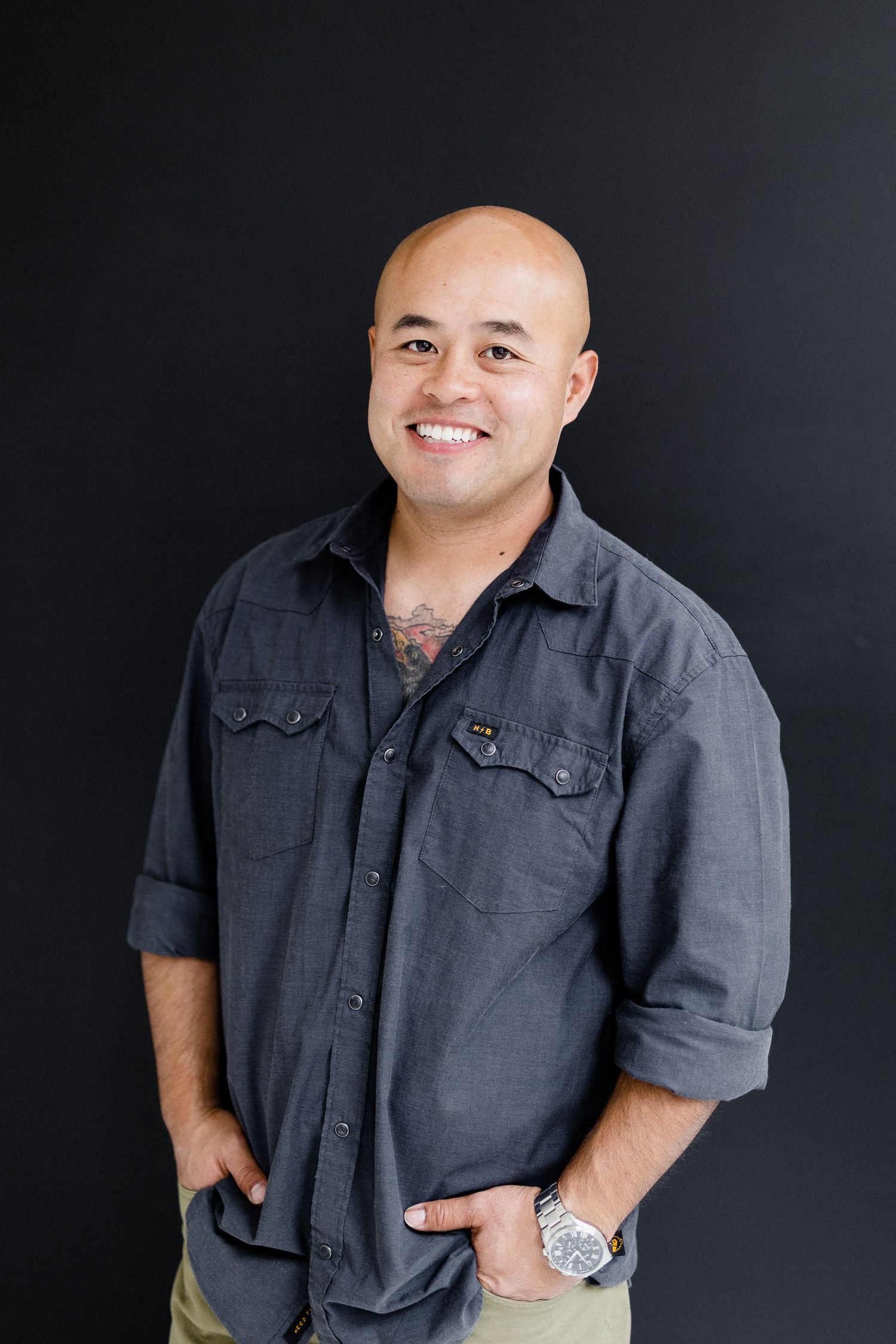 Portrait of photographer in gray button-up shirt against black background.