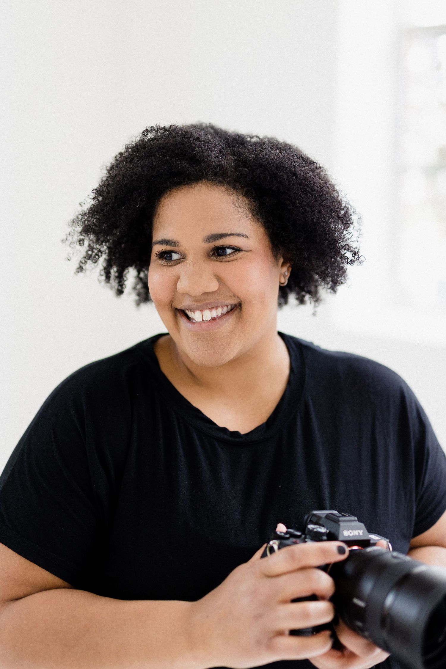 Portrait of photographer with natural hair holding camera in bright studio setting.