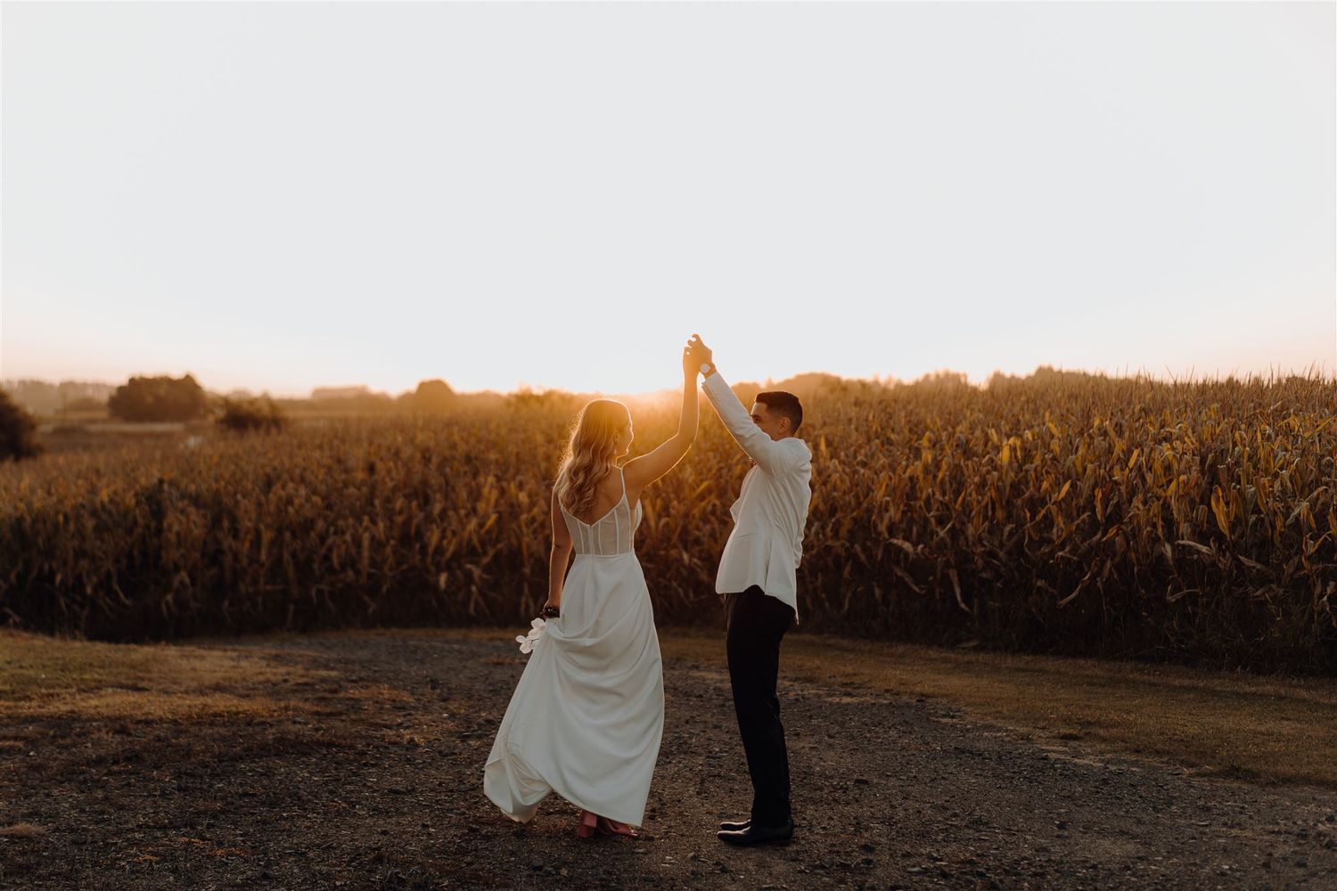 Bride and groom dancing at sunset in front of a cornfield