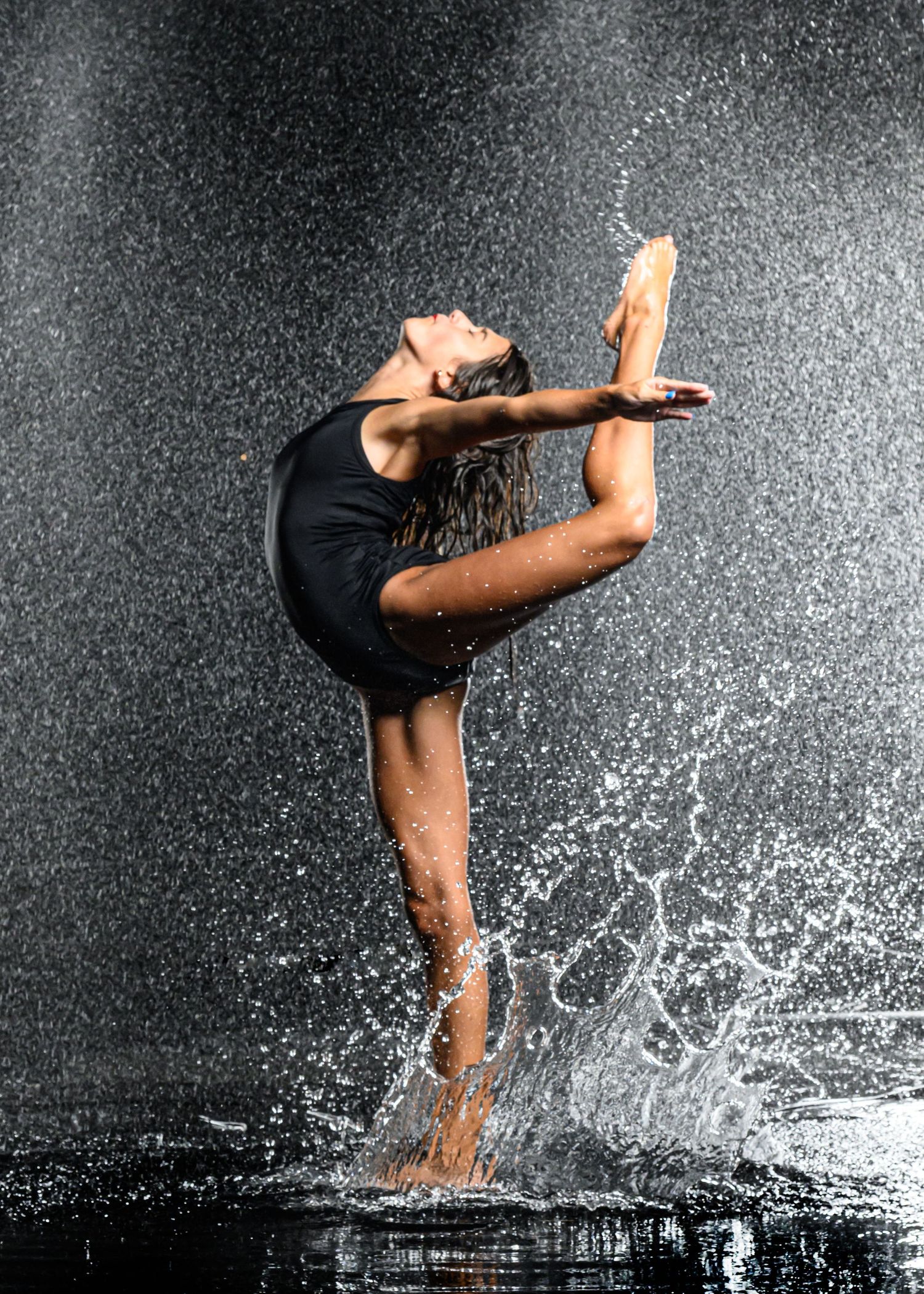 Dancer in black leotard executing dramatic split pose with water splash effects.