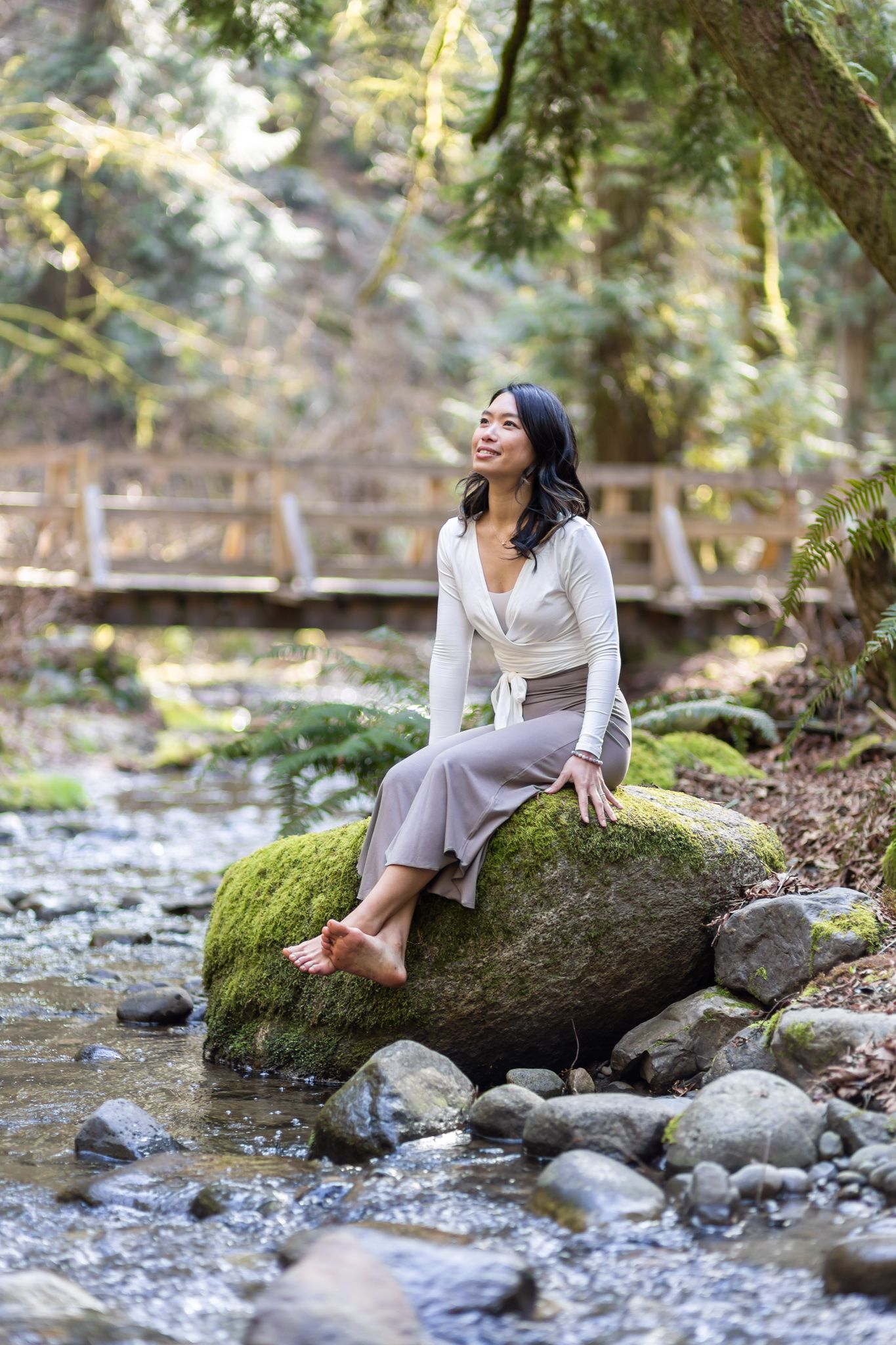 yoga instructor personal branding photos in Kirkland, WA woman sitting on rock by river looking up surrounded by forest 