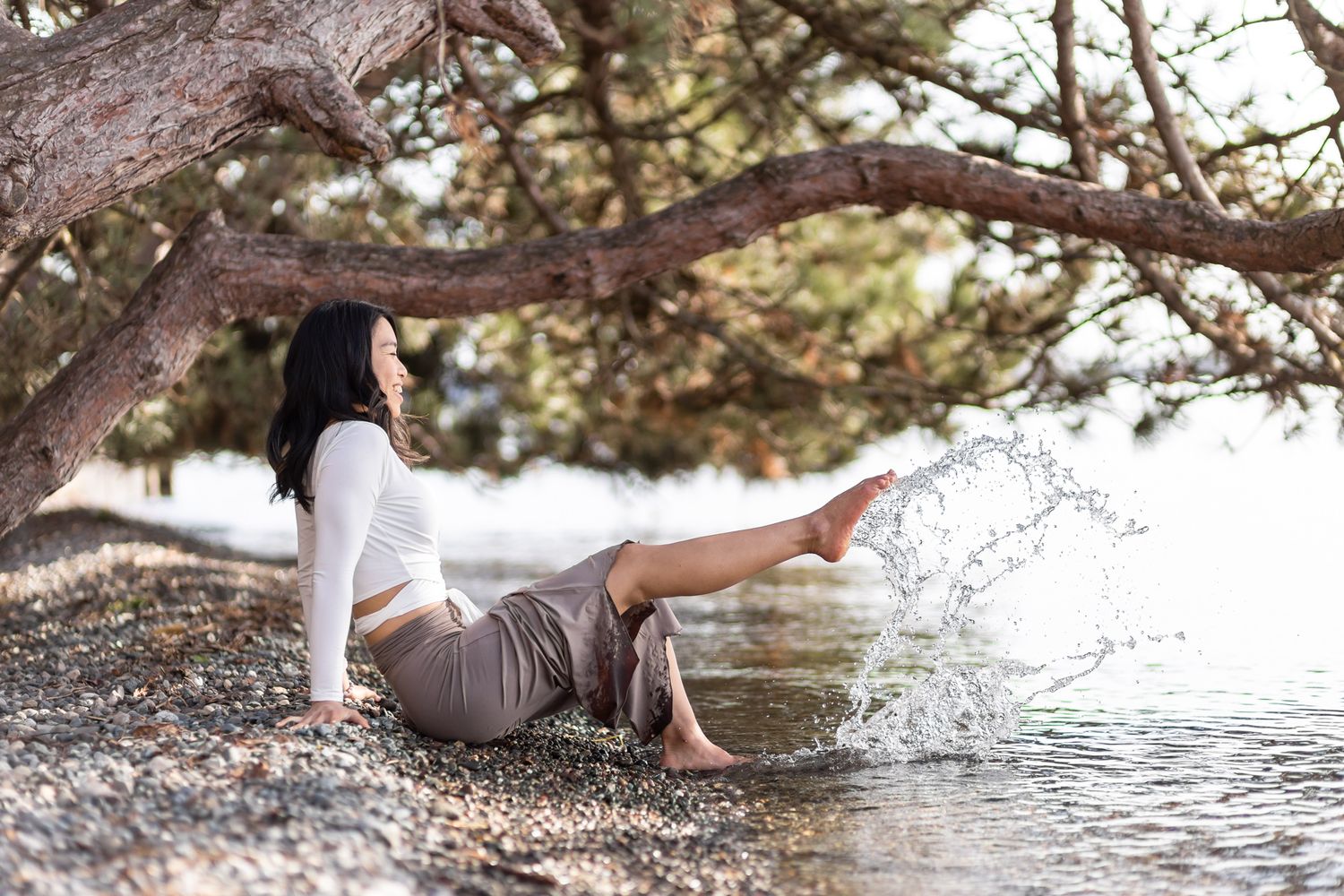 yoga instructor personal branding photos in Kirkland, WA woman sitting on rocks by ocean under tree playing with water