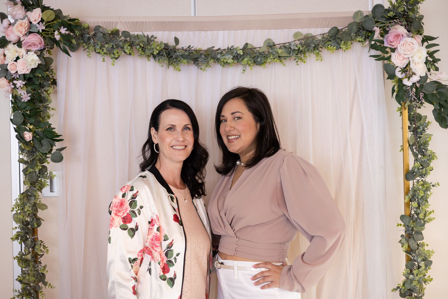 The Divine Pearl Collective event photography in Edmonds, WA 2 women owners smiling at camera in front of floral backdro