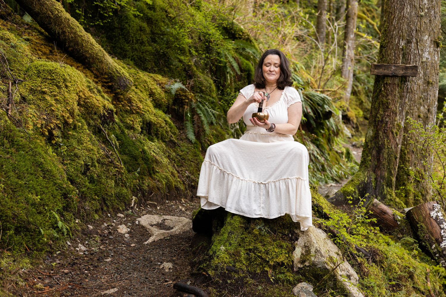 woman spiritual business owner branding photos in North Bend, WA sitting on stump playing sound bowl reiki healer