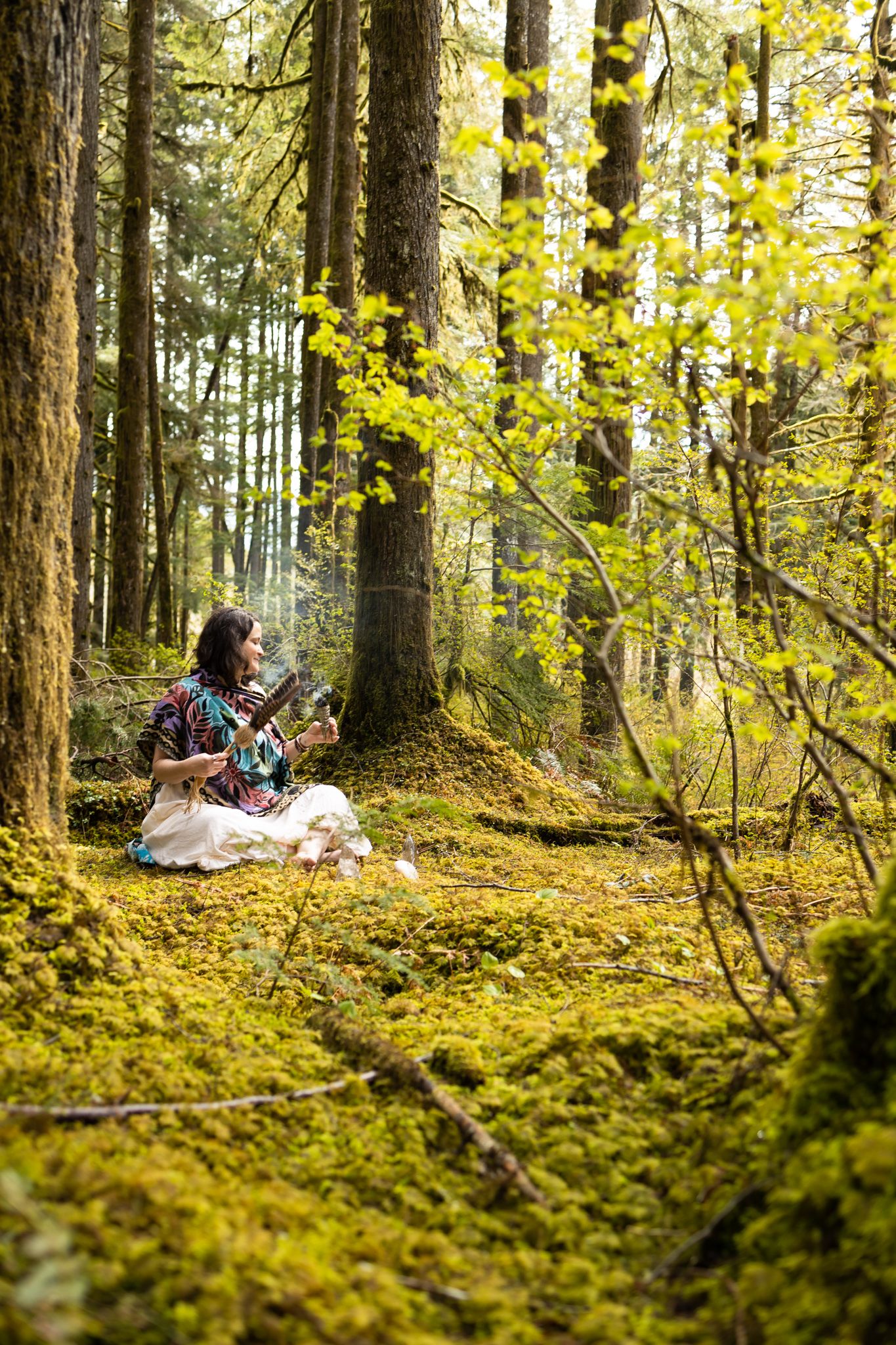 woman spiritual business owner branding photos in North Bend, WA sitting in mossy forest burning cleansing herbs with fe