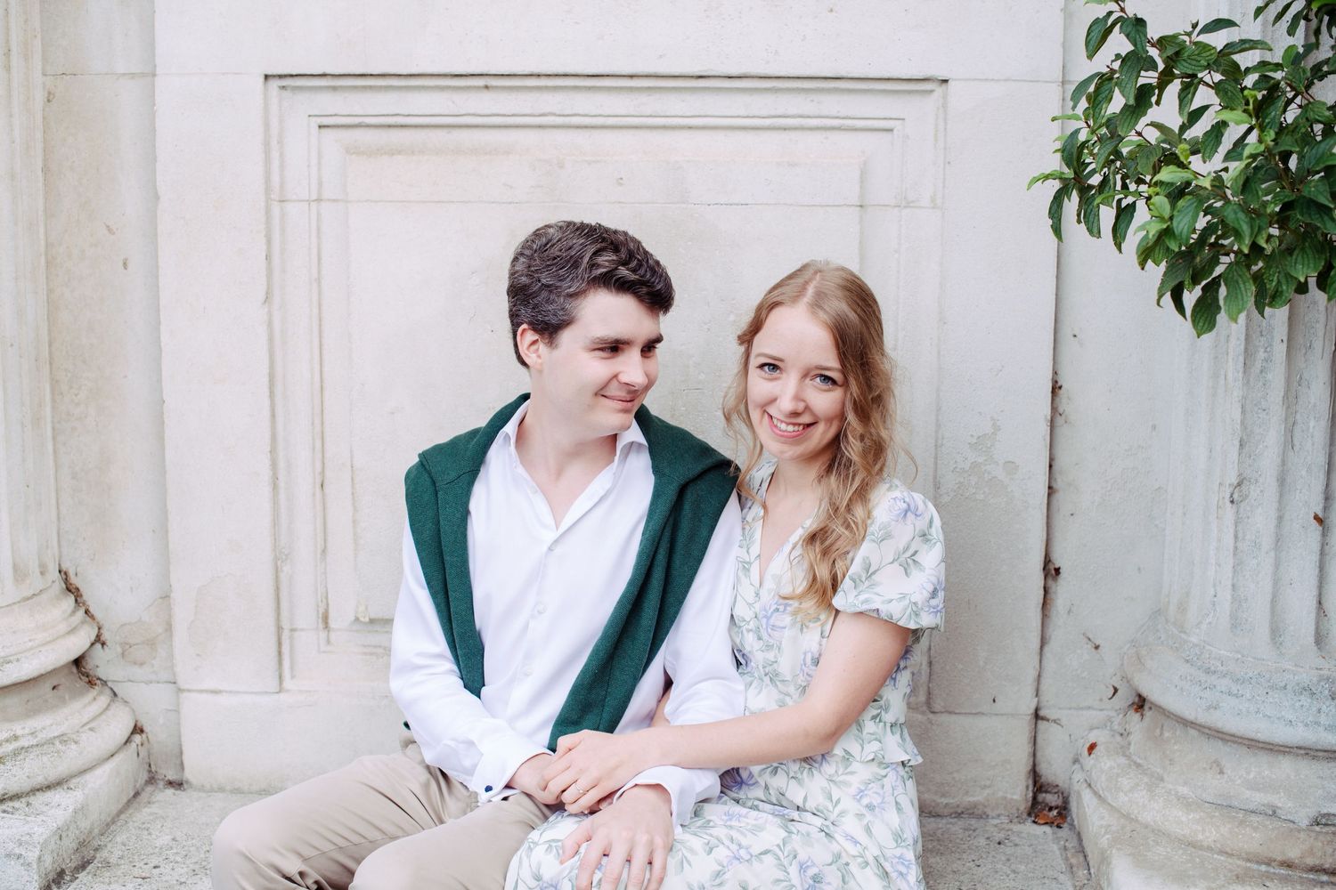 A couple sits together on stone steps outdoors, with one wearing a green cardigan and white shirt.