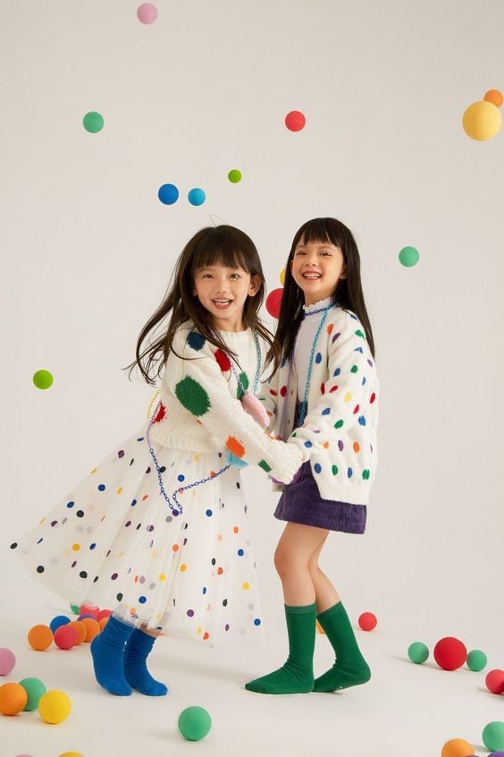 Two children in polka dot outfits playing with colorful balls against a white background.