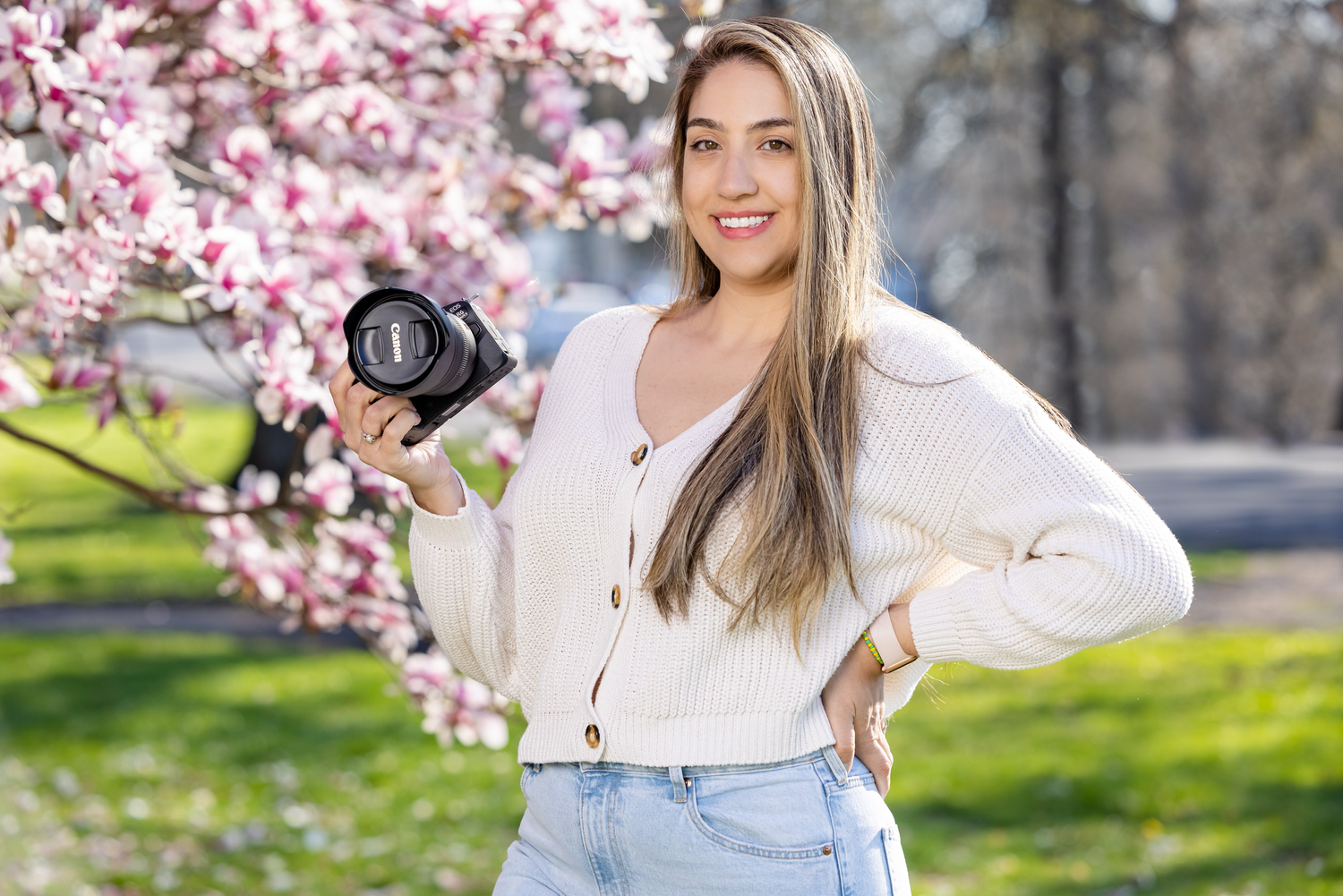 Photographer posing with camera near blooming cherry blossoms in springtime.