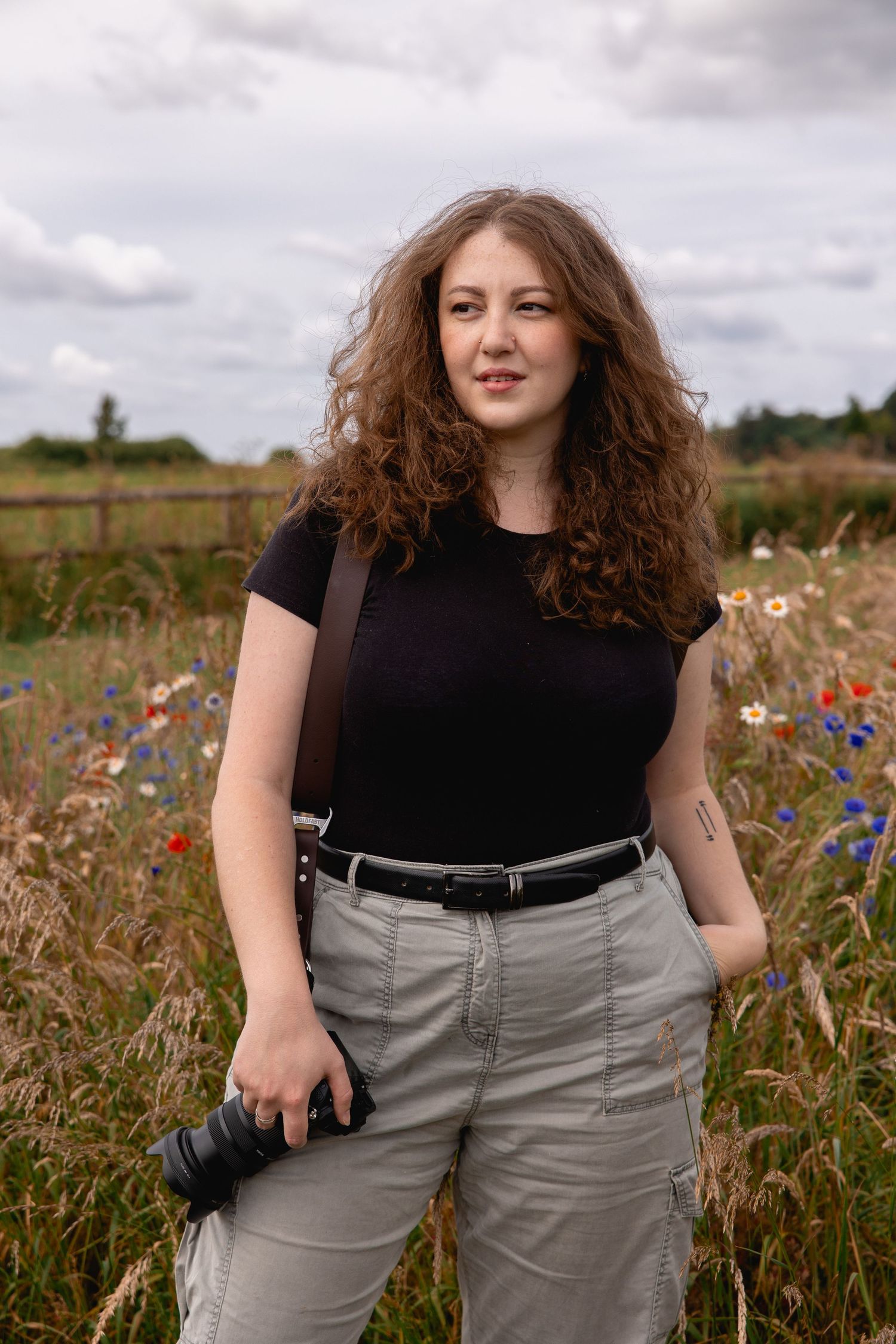 Ampersand Memories Photography owner gazes into the distance, camera in hand, amidst a wildflower field