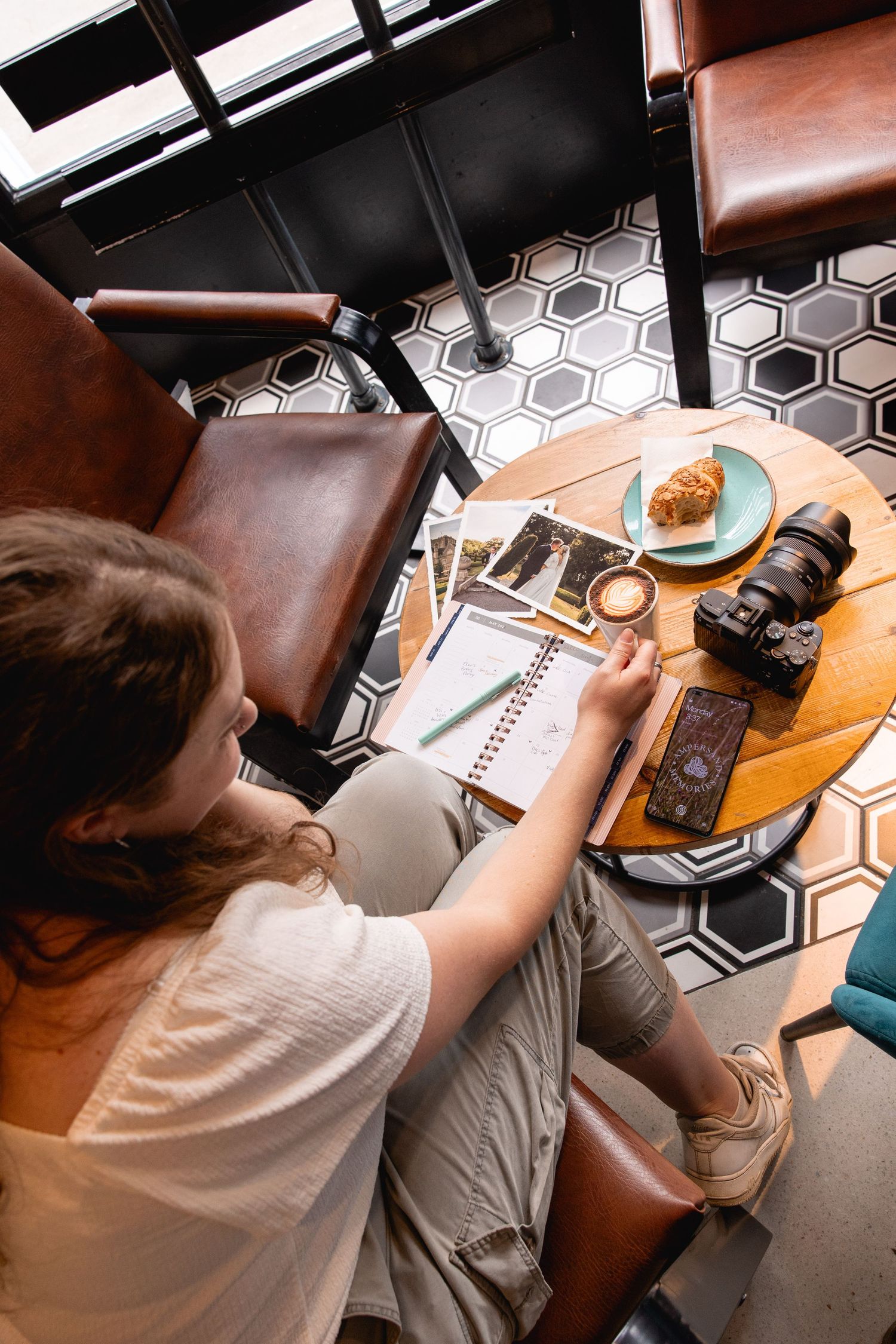 Overhead view of workspace with leather chairs, camera gear, and notebook on hexagonal tile floor.