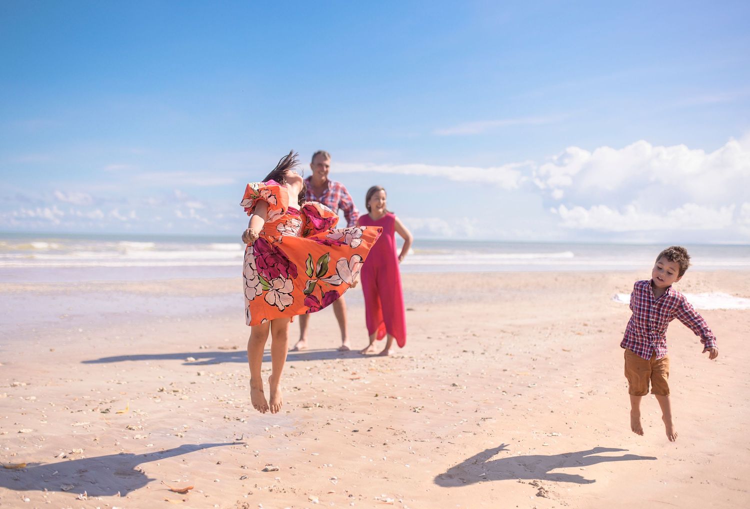 People in colorful dresses dance and play on a sunny beach.