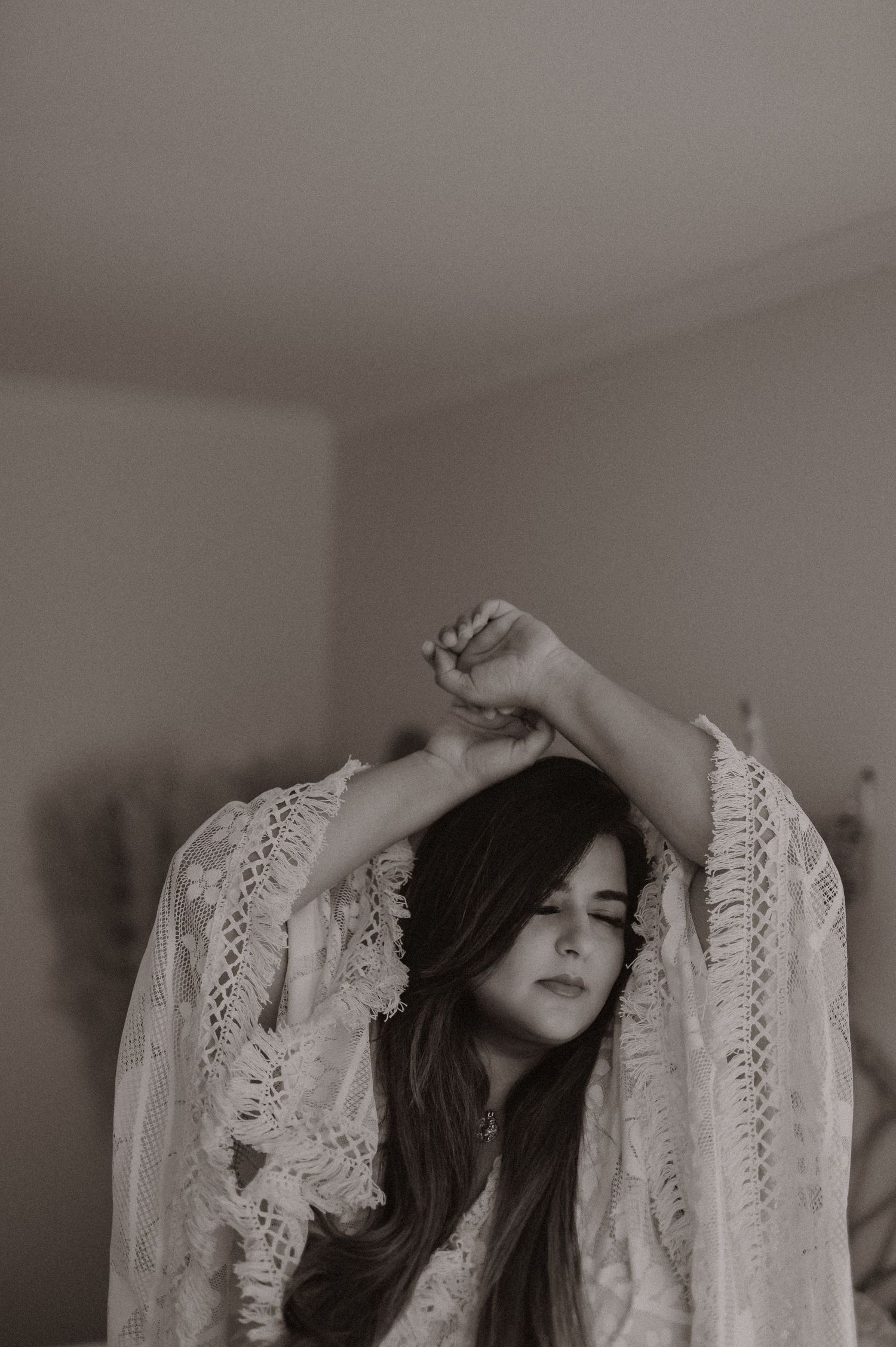 Artistic black and white portrait of woman in lace dress with raised arms.