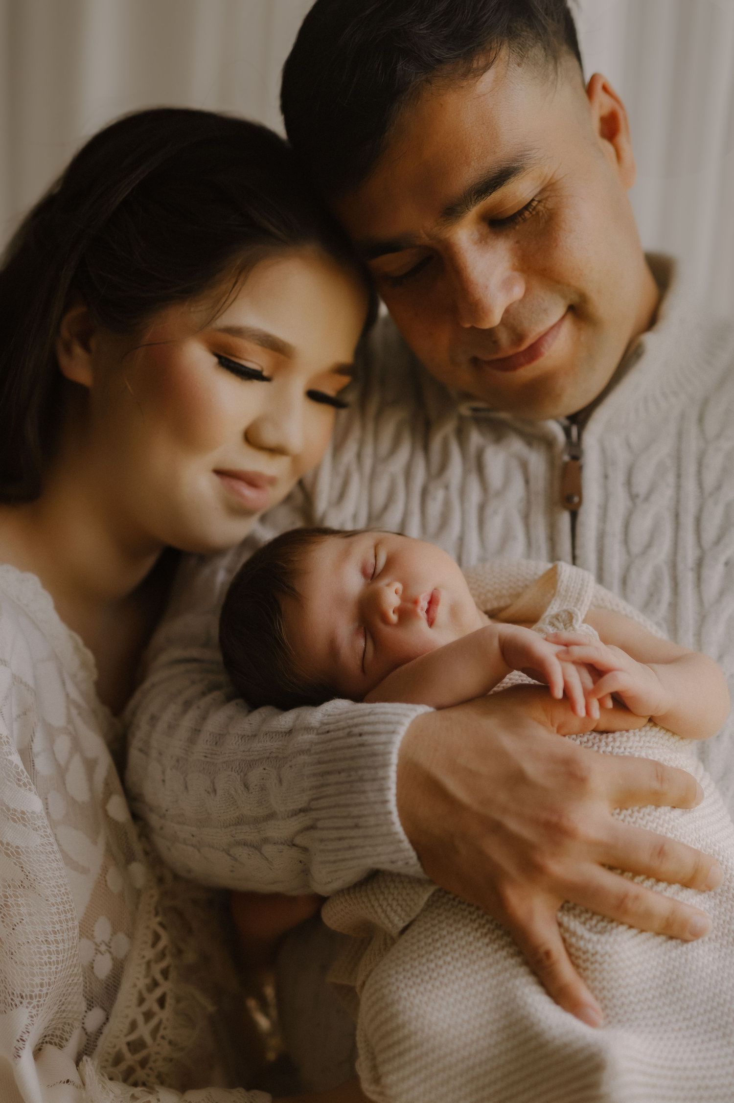 A tender family moment as parents in cozy sweaters cuddle their sleeping newborn baby.