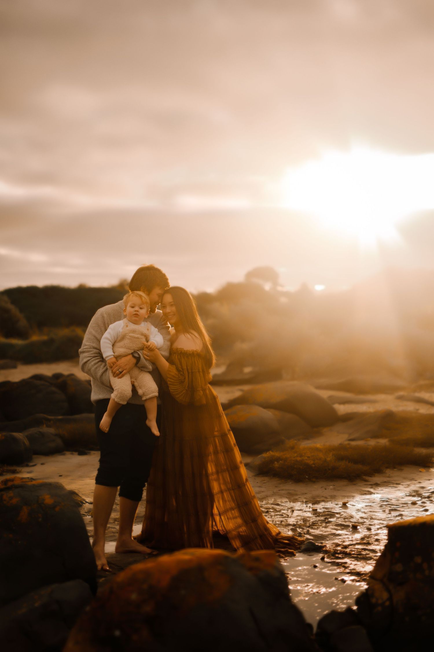 Family embracing on rocky beach during golden hour sunset.