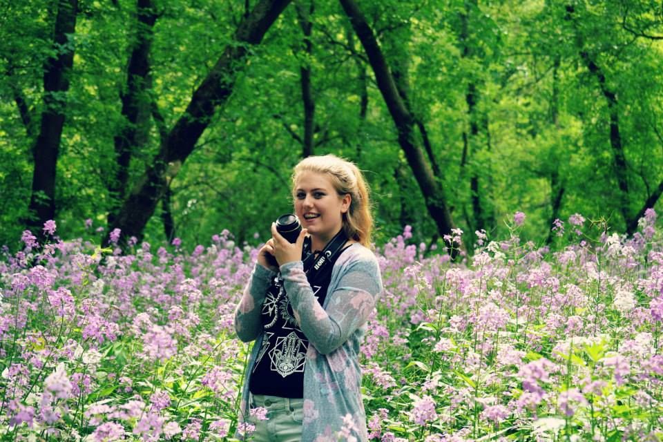 A photographer capturing images among purple wildflowers in a green forest setting.