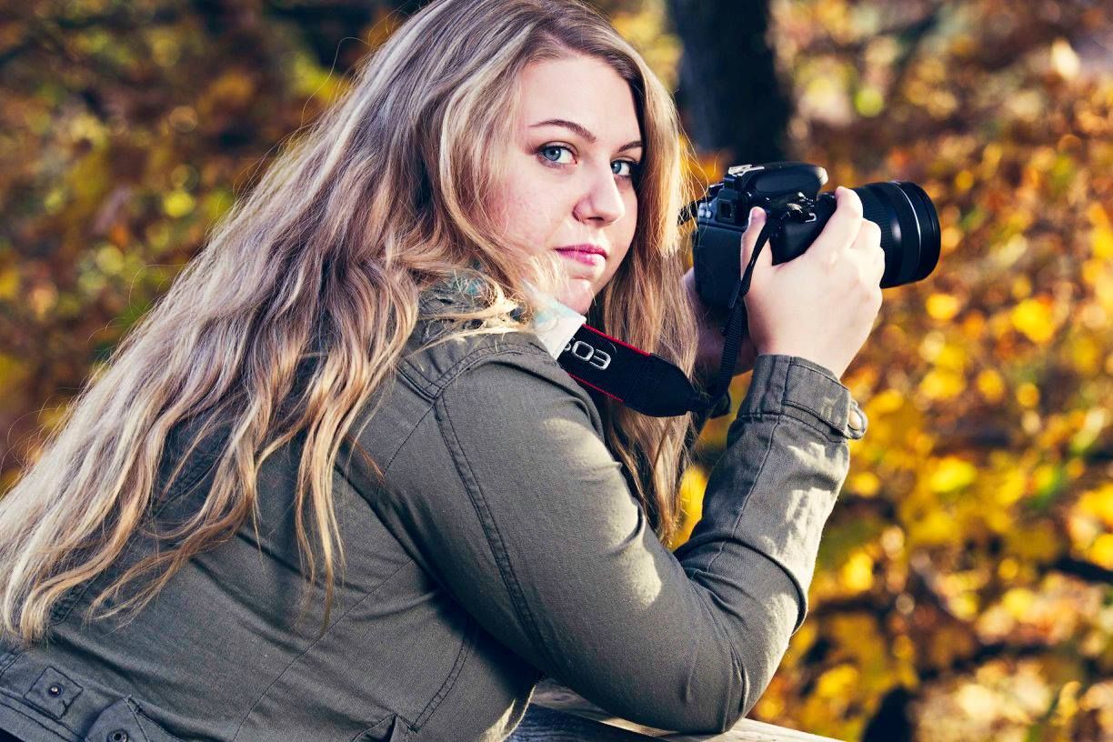 A photographer with a professional camera against an autumn background of golden leaves.