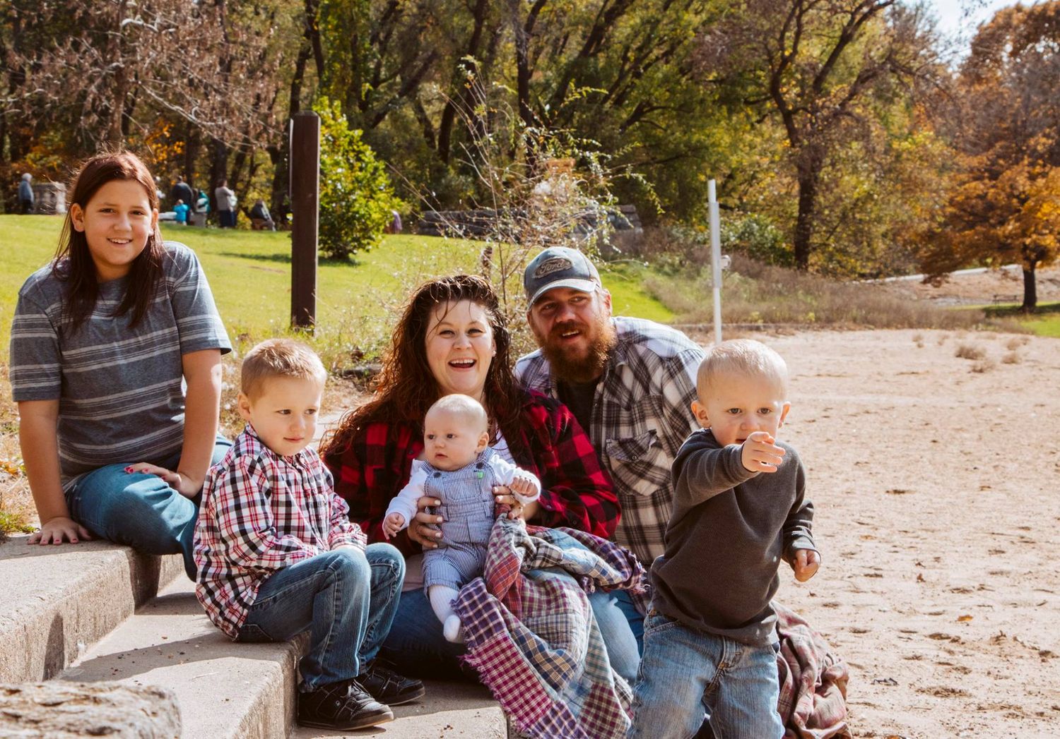 Family group sitting together on stone steps during autumn in a park setting.