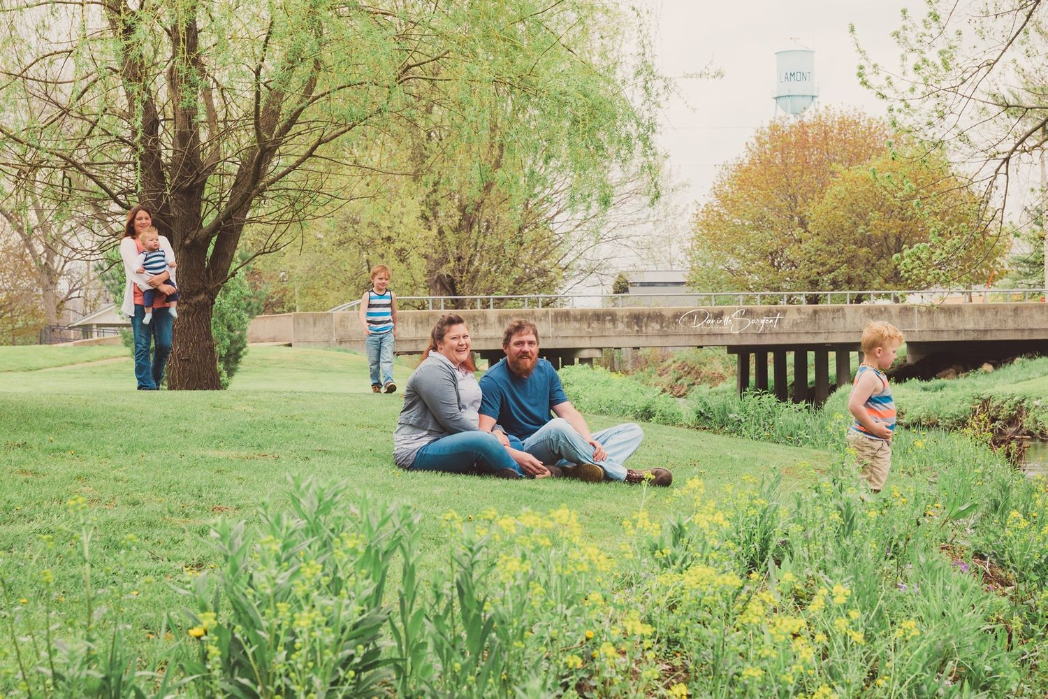 Family spending leisure time in spring park with flowering yellow wildflowers and stone bridge.