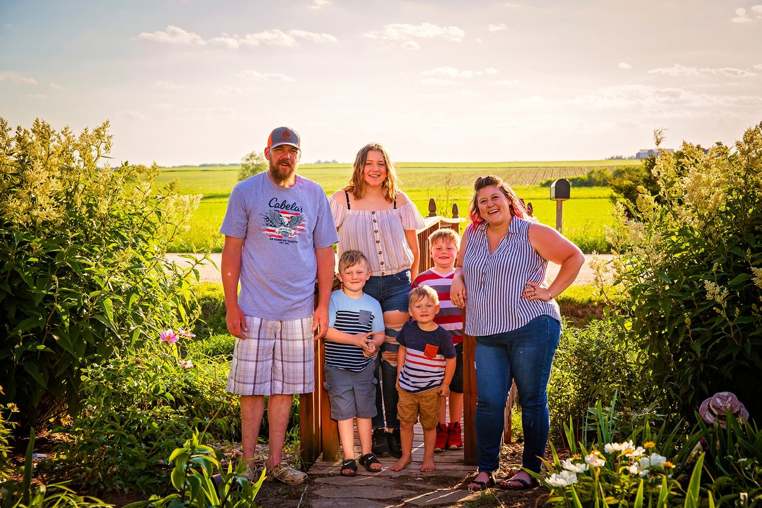 Family standing together on nature trail surrounded by summer wildflowers at sunset.