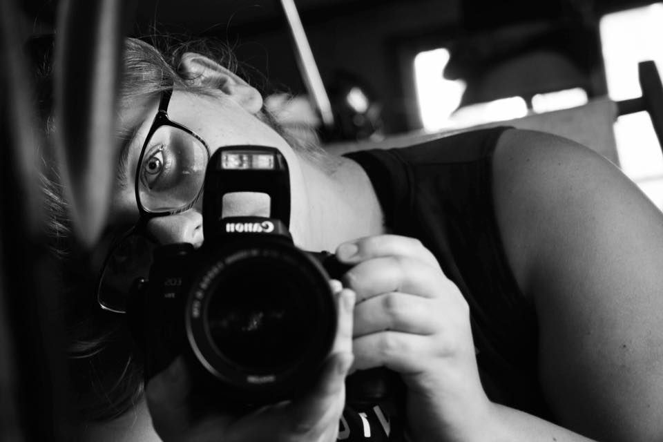 A close-up black and white photo of someone looking through a camera lens.