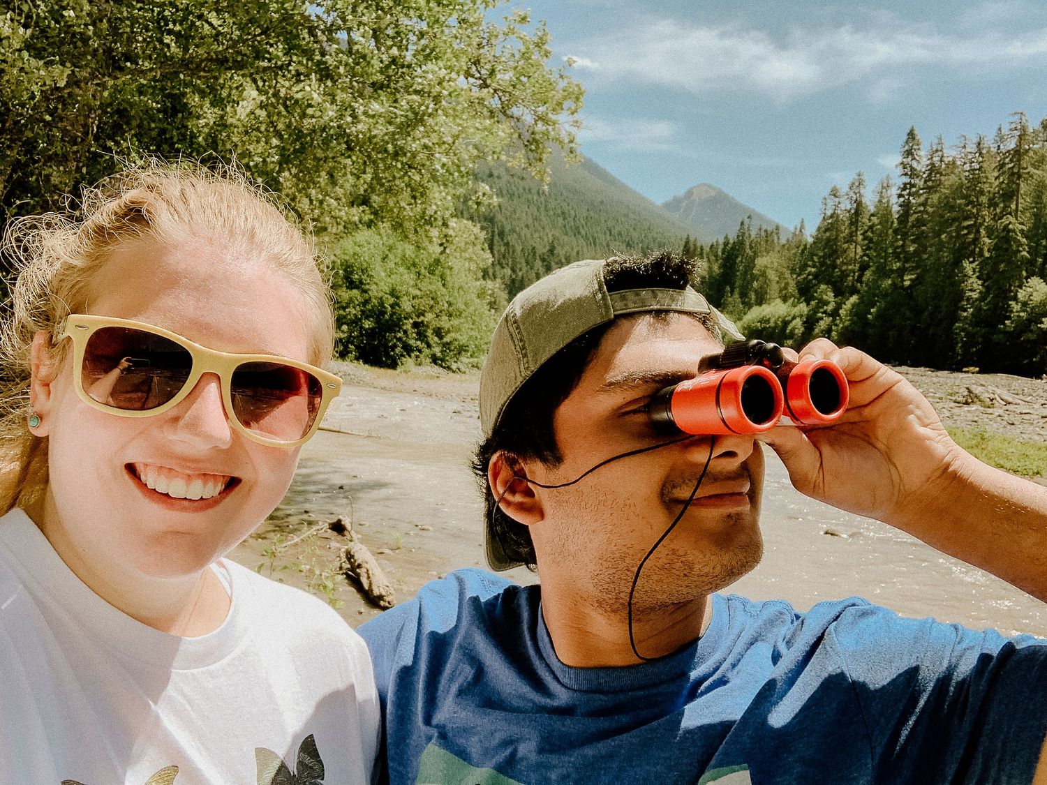 Two people enjoying outdoor adventure with binoculars against mountain backdrop.