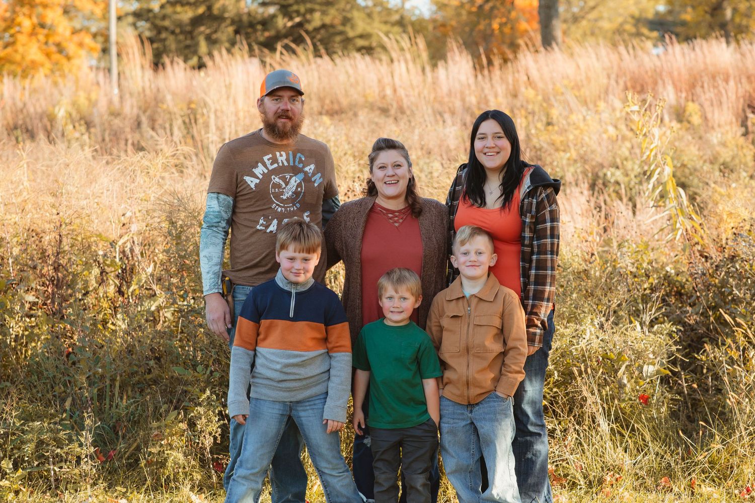 Family portrait in golden autumn field with tall grass and warm sunset lighting.