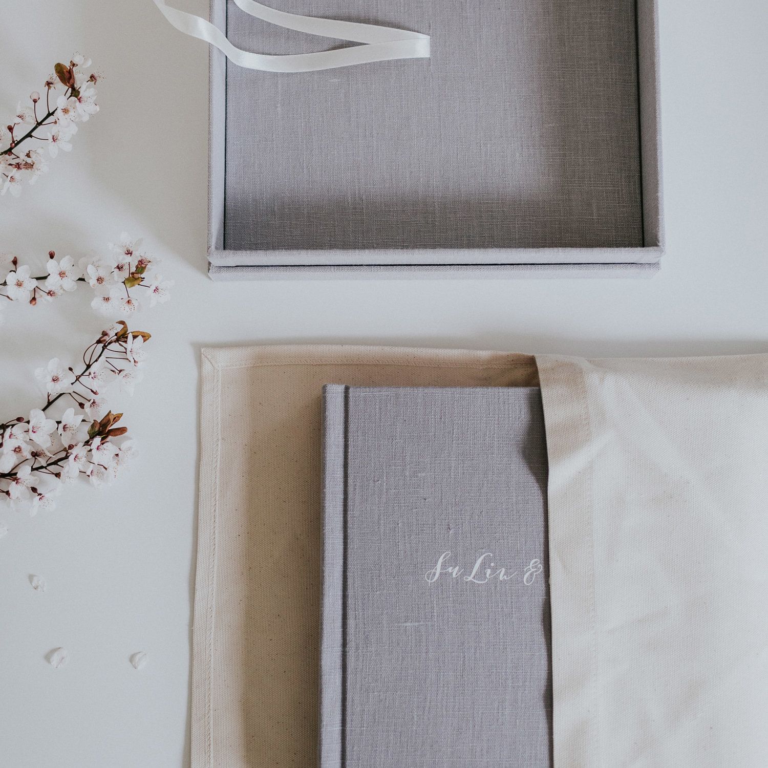 Elegant gray linen wedding album cover styled with delicate cherry blossom branches.