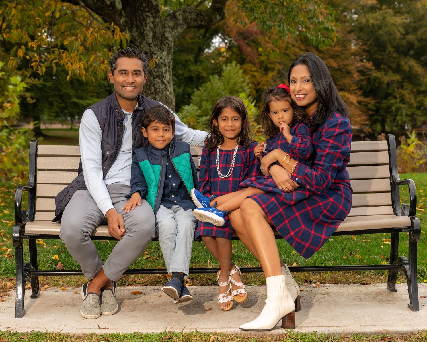 Family sitting together on a park bench surrounded by autumn foliage.